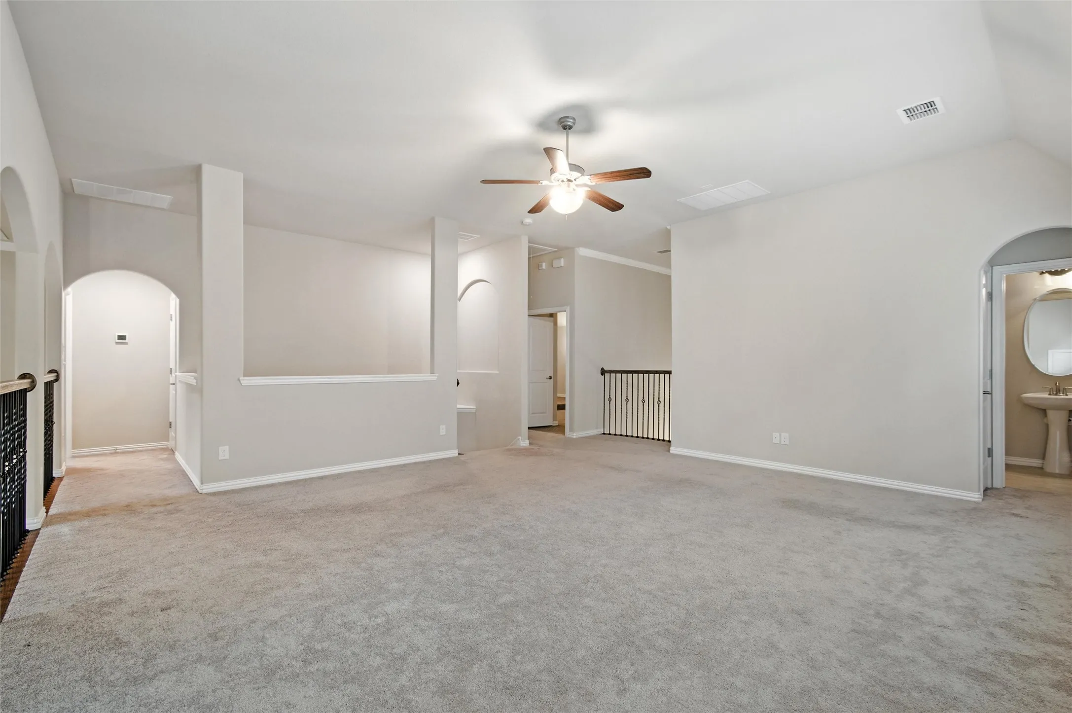 Unfurnished living room featuring arched walkways, light carpet, and ceiling fan