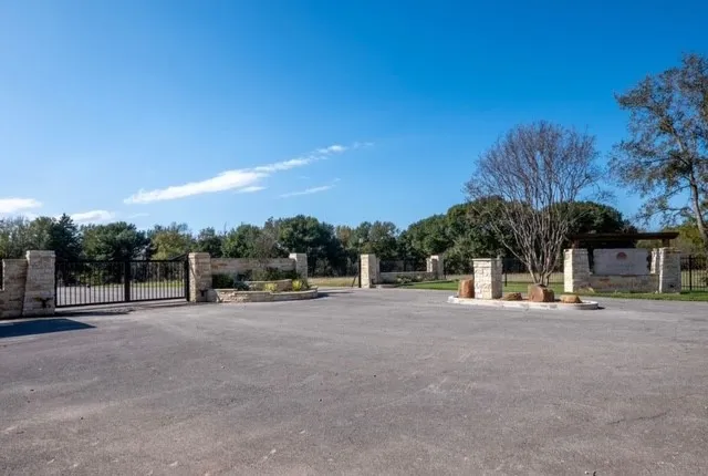 View of asphalt street featuring a gate, a gated entry, and curbs