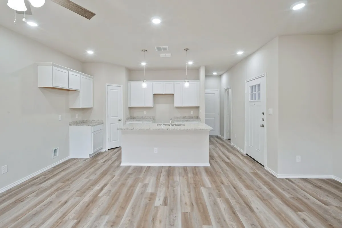 Kitchen with light wood-type flooring, a kitchen island with sink, recessed lighting, white cabinets, and light stone countertops