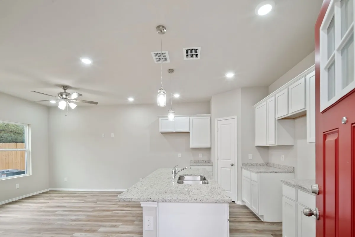 Kitchen with light wood-style floors, decorative light fixtures, light stone counters, a center island with sink, and recessed lighting