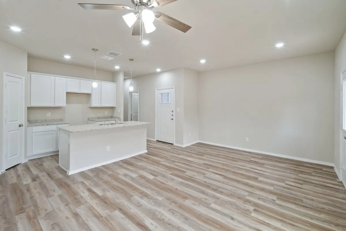 Kitchen featuring an island with sink, light wood finished floors, light stone counters, white cabinetry, and recessed lighting
