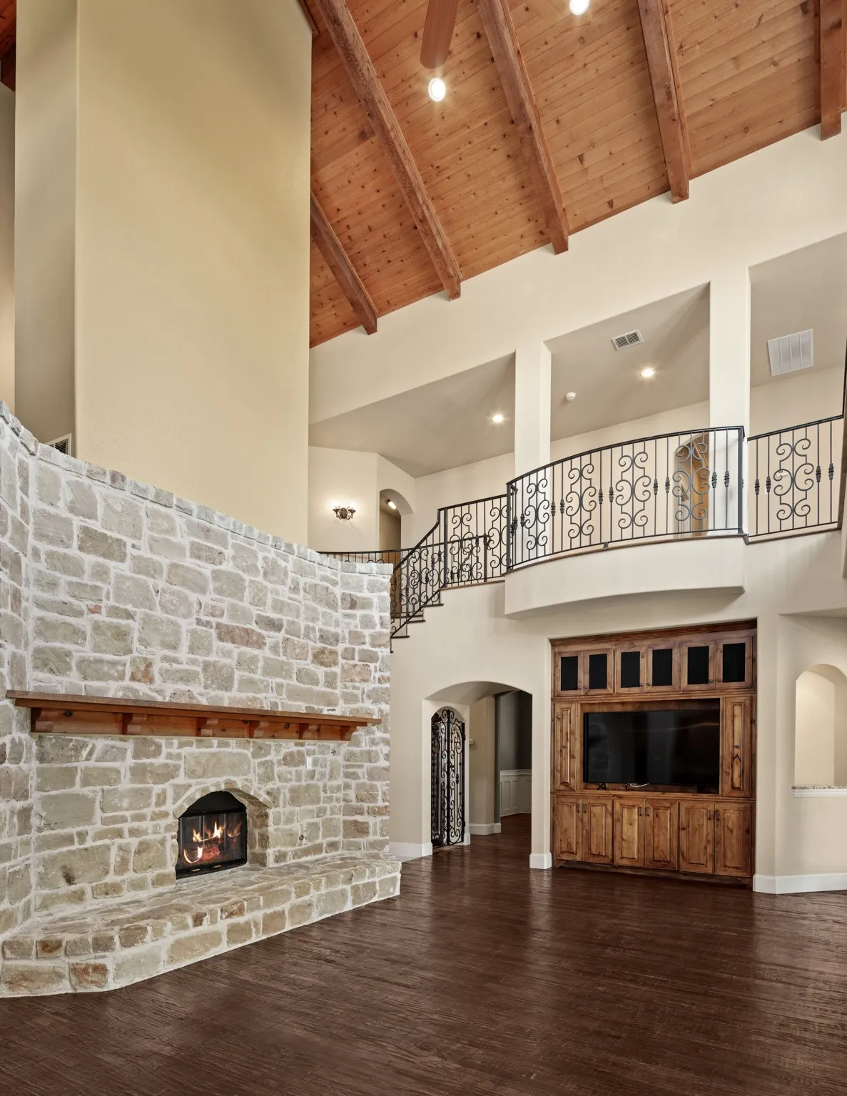 Enhancing the grandeur of the main living area is a soaring vaulted wood-beamed ceiling, adding architectural drama and a touch of rustic elegance that perfectly complements the Tuscan-inspired design. A stunning wrought iron staircase ascends gracefully to the second level, where ornate ironwork continues across arched bridges and a beautifully gated gallery edge—seamlessly uniting form and function while echoing the timeless craftsmanship and old-world charm that define this exceptional estate.