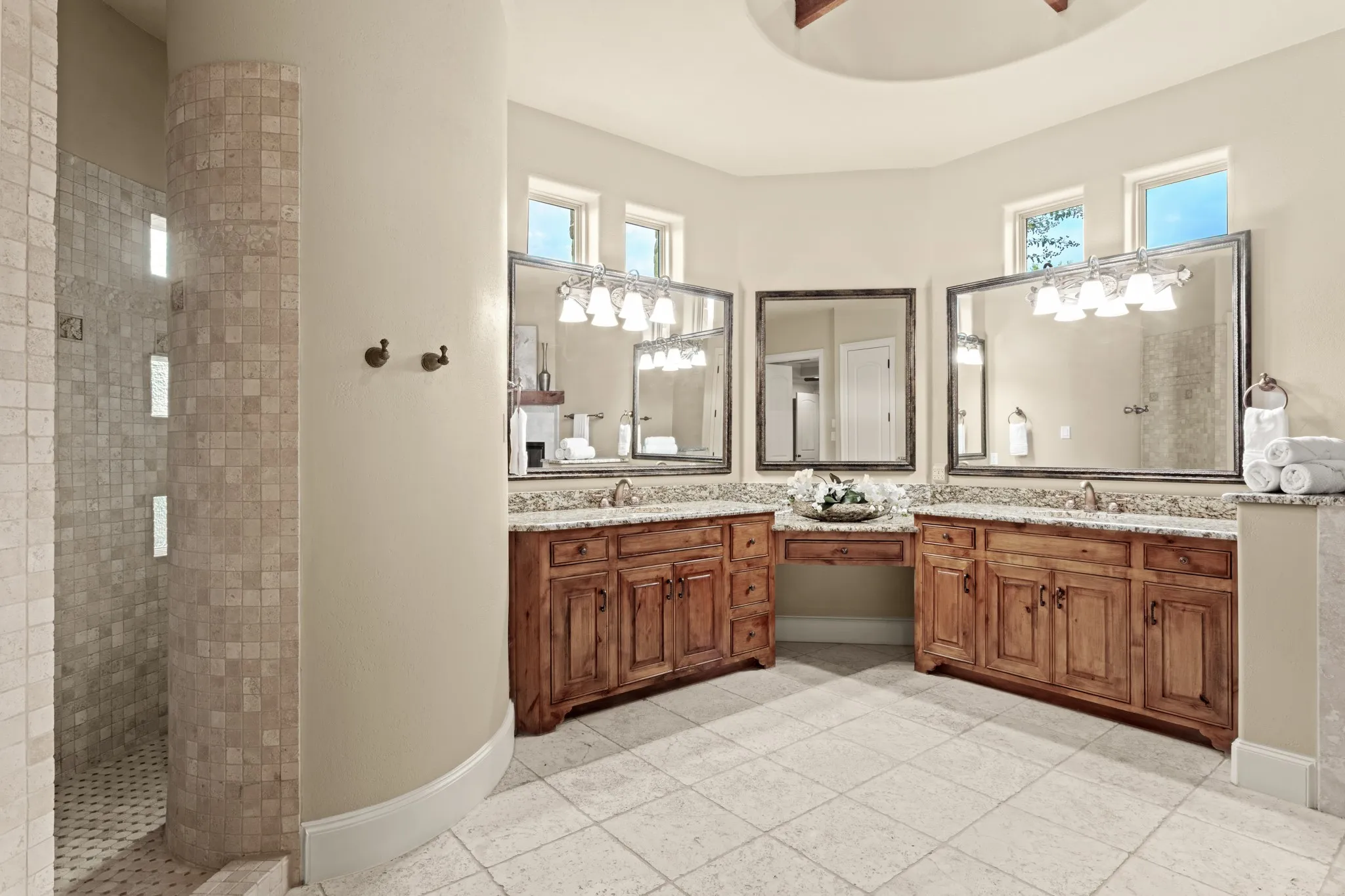 Step into this exquisite master suite bath, where elegance meets comfort. Featuring dual granite vanities with rich wooden cabinetry, this space offers ample storage and a sophisticated aesthetic. The curved walk-in double shower is adorned with a stunning travertine surround, providing a spa-like experience with its unique design. Complementing the shower, the travertine floors add a seamless and timeless touch of luxury. To complete this serene retreat, a raised oversized jetted tub invites you to soak away the worries of the day, making this bathroom a true sanctuary of relaxation and style.