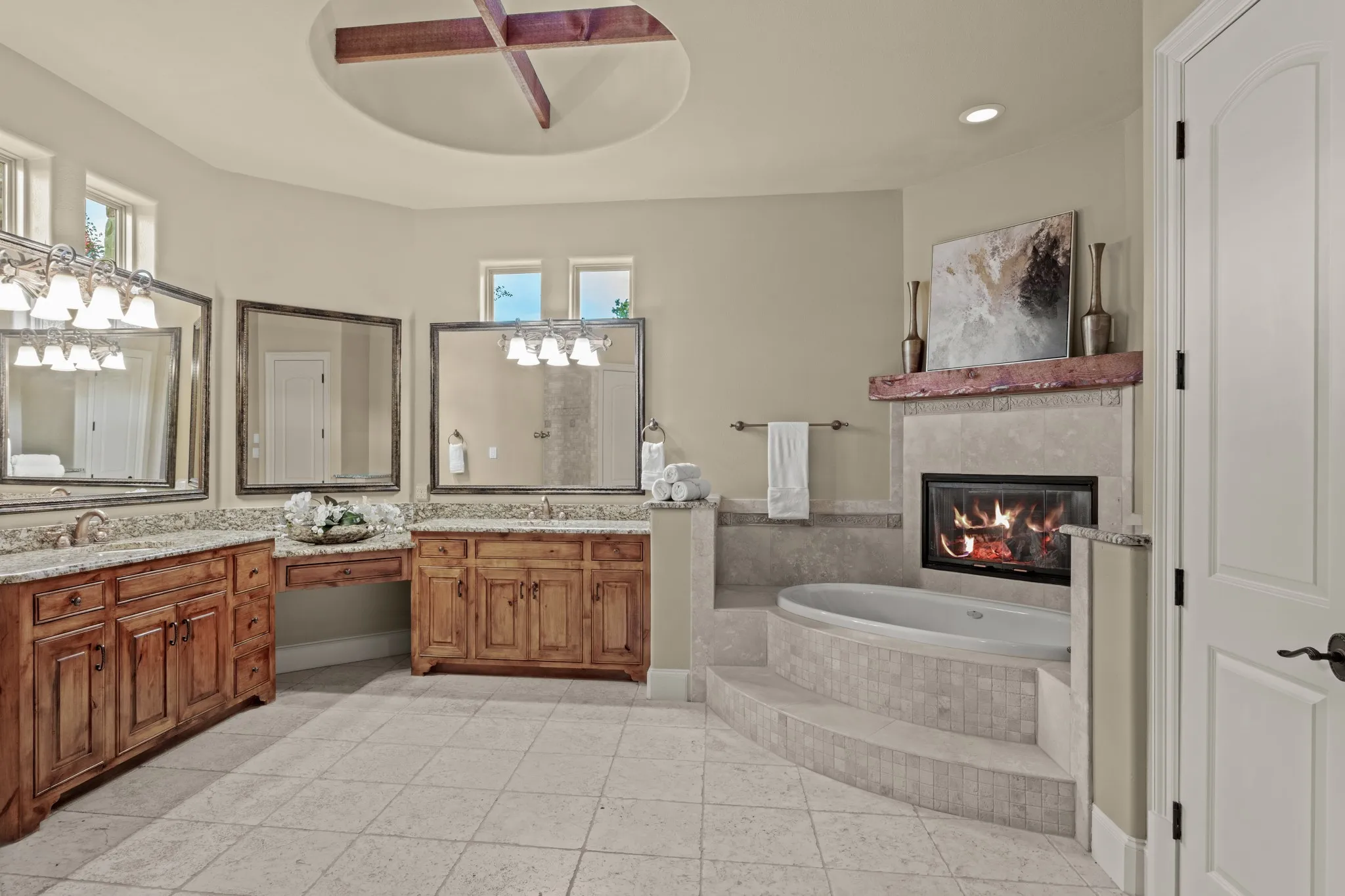 Step into a spa-inspired sanctuary designed for ultimate relaxation and refinement. This exquisite owner’s bathroom boasts a show-stopping ceiling feature with rustic beam accents, setting the tone for elevated luxury. A deep jetted soaking tub is perfectly positioned beside a cozy fireplace, creating a tranquil retreat for unwinding in style. Dual granite-topped vanities offer ample space and elegance, while a beautifully tiled, oversized double shower adds both function and flair. Travertine flooring flows throughout, enhancing the timeless appeal. A massive walk-in closet with two separate sides completes this exceptional space, offering abundant storage and everyday convenience.