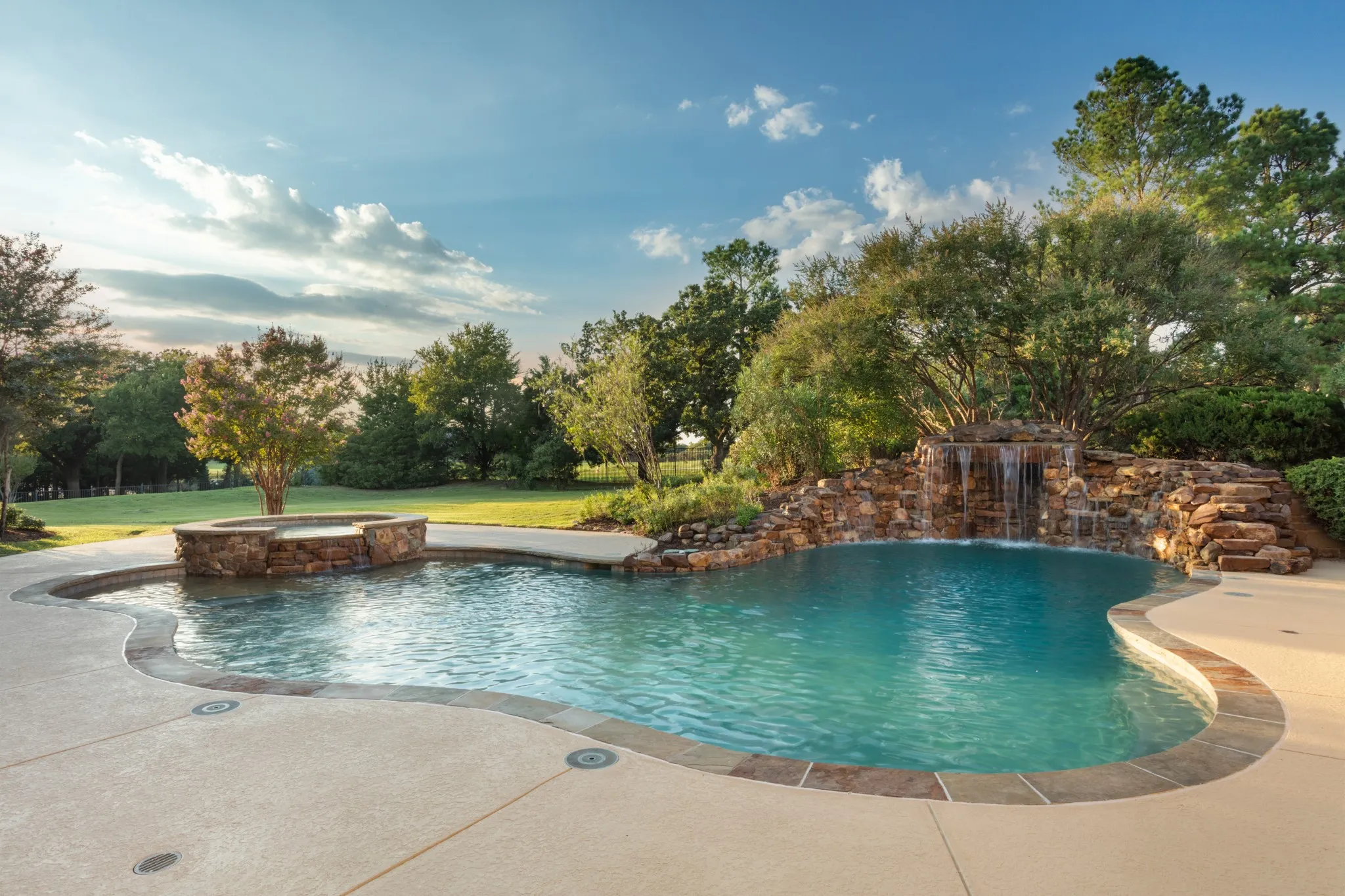 An Outdoor Retreat Like No Other. Nestled on 2 lush, private acres in the heart of Texas, this custom-designed pool area redefines resort-style living. At the heart of the retreat lies a stunning 35,000-gallon pool, complete with a natural rock waterfall grotto—creating a serene, cave-like escape. With depths reaching 9 feet, the pool is perfectly designed for thrilling jumps from the top of the grotto, while the gradual 3 to 4.5-foot shallows provide a relaxing space to float or lounge. An expansive tanning ledge offers the ideal spot for in-water loungers, allowing you to soak up the sun in comfort and style. Surrounded by mature trees and thoughtfully landscaped grounds, this outdoor haven offers unmatched privacy, tranquility, and luxury—all in your own backyard.