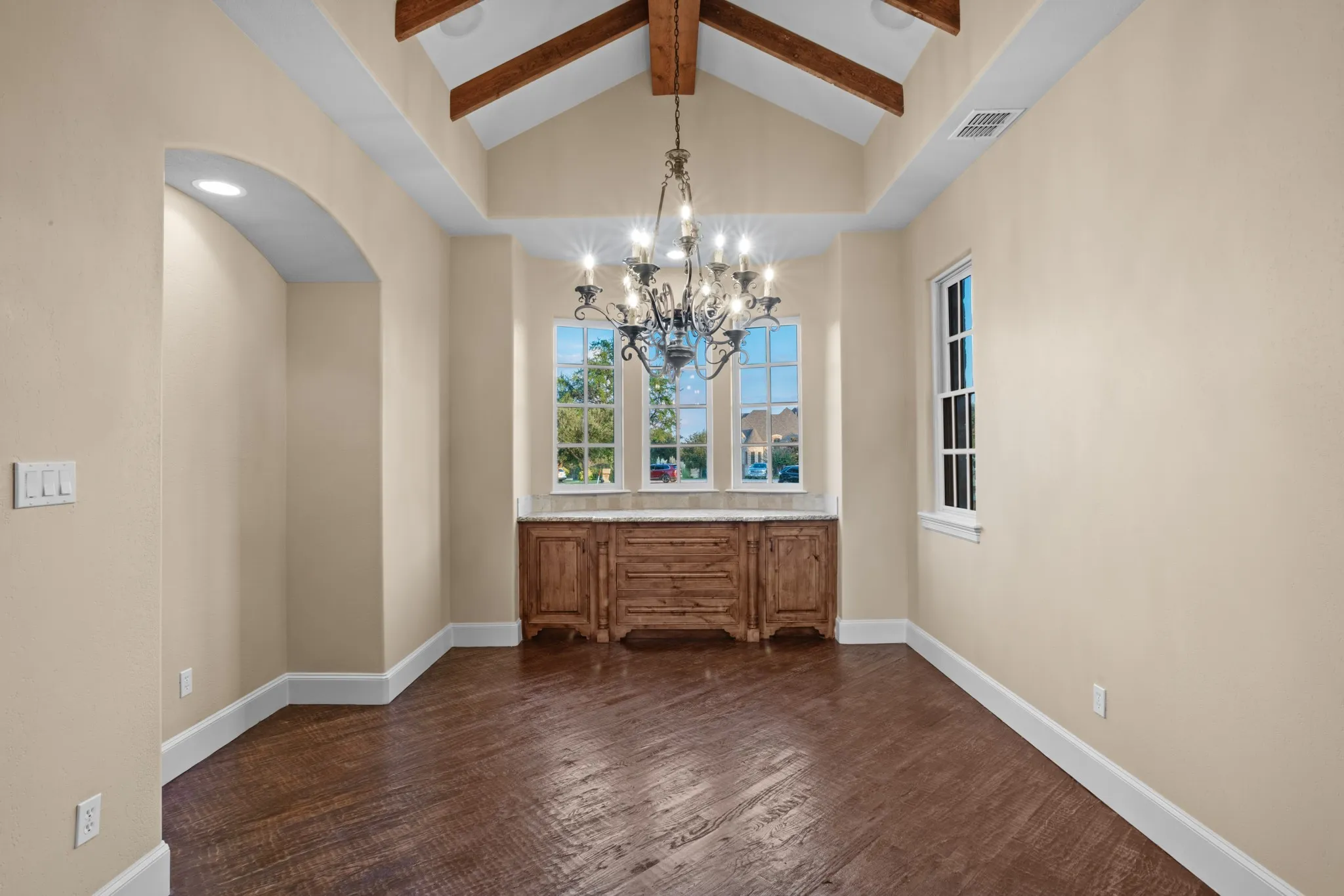 This stunning main dining area in a multi-million dollar estate exudes timeless elegance with its hand-scraped wood floors that add warmth and character. The vaulted ceiling with exposed wooden beams creates an airy and grand atmosphere, perfectly complemented by a forged iron chandelier that serves as a striking focal point. Adjacent to the dining space, a convenient butler's pantry with rich wood cabinetry and granite countertops offers both functionality and style, making this room ideal for both intimate dinners and grand entertaining.