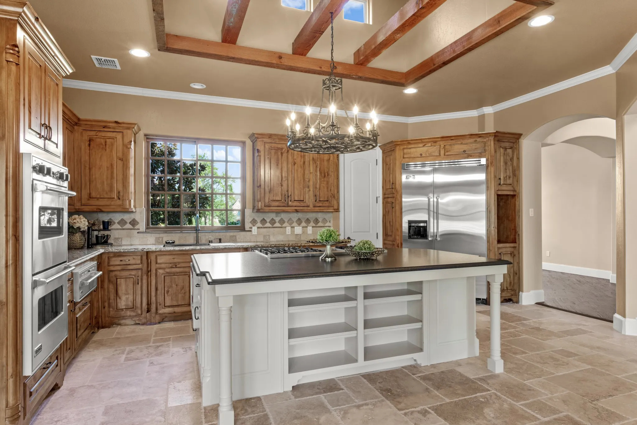 This extraordinary chef’s kitchen must be experienced in person to fully appreciate its scale, craftsmanship, and design. At its heart lies a massive leathered granite island with an extended breakfast bar—both a striking centerpiece and a functional workspace. Soaring ceilings are accented with rich cedar detailing, drawing the eye upward to a row of sleek pocket windows that bathe the space in natural light. Double ovens provide culinary versatility, while brand-new travertine floors flow seamlessly into the coordinating travertine backsplash, creating a cohesive and refined aesthetic throughout.