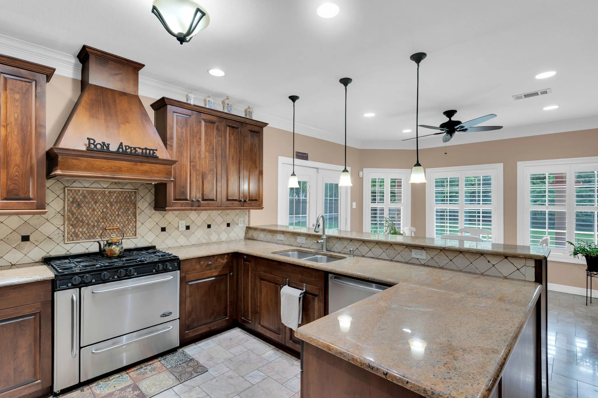 Kitchen with a peninsula, stainless steel appliances, light stone countertops, custom exhaust hood, and hanging light fixtures