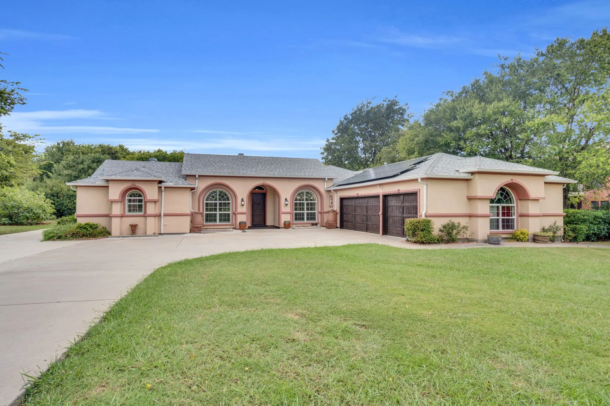 Mediterranean / spanish-style house with stucco siding, roof mounted solar panels, concrete driveway, an attached garage, and a front lawn