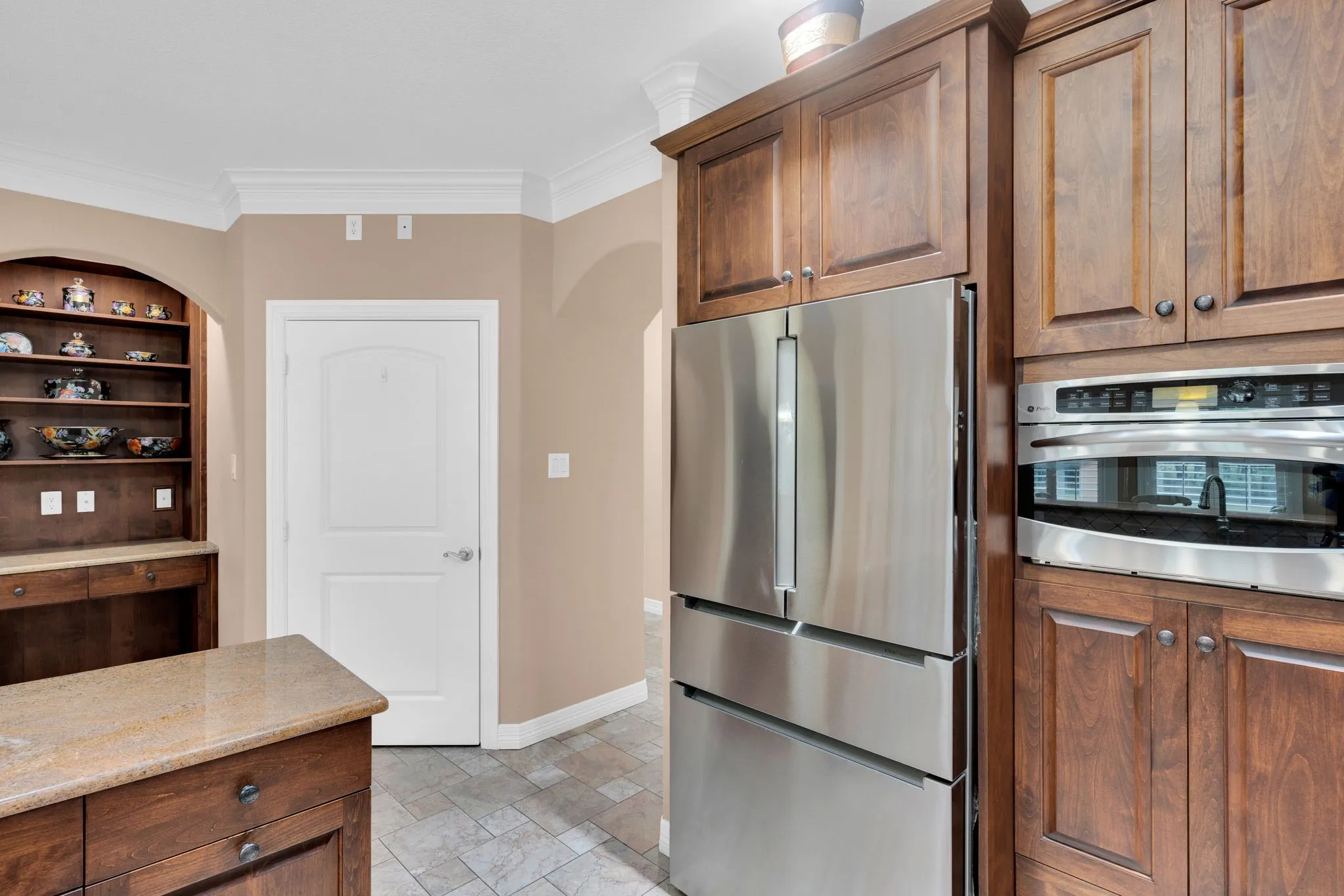 Kitchen featuring stainless steel appliances, crown molding, light stone finish floors, light stone countertops, and brown cabinetry