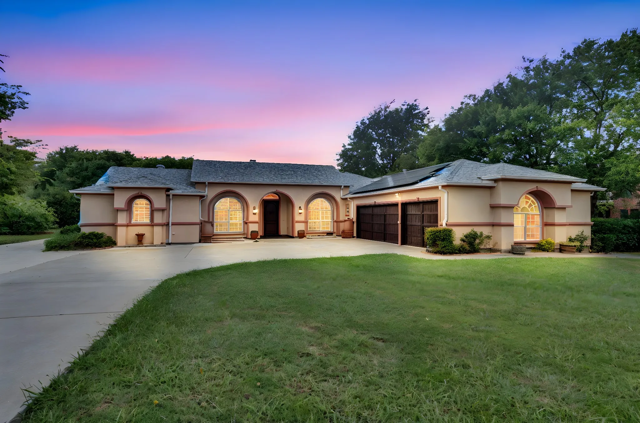 View of front of home with stucco siding, a garage, concrete driveway, solar panels, and a yard