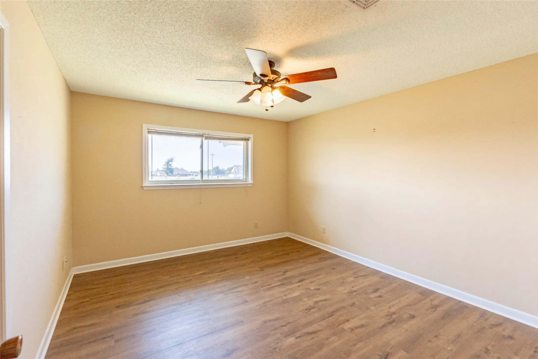 Empty room featuring a textured ceiling, wood finished floors, and a ceiling fan