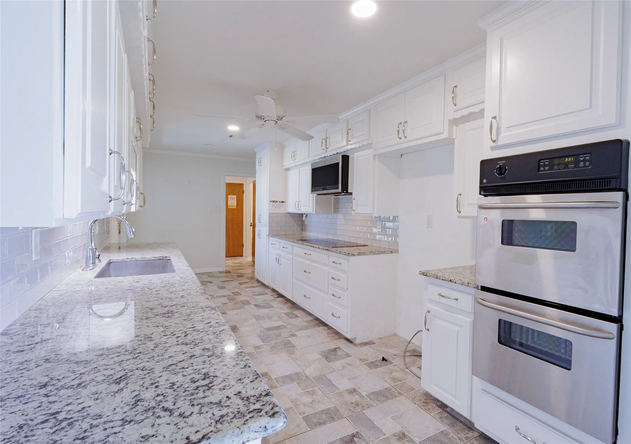 Kitchen with stainless steel appliances, decorative backsplash, white cabinets, light stone counters, and recessed lighting