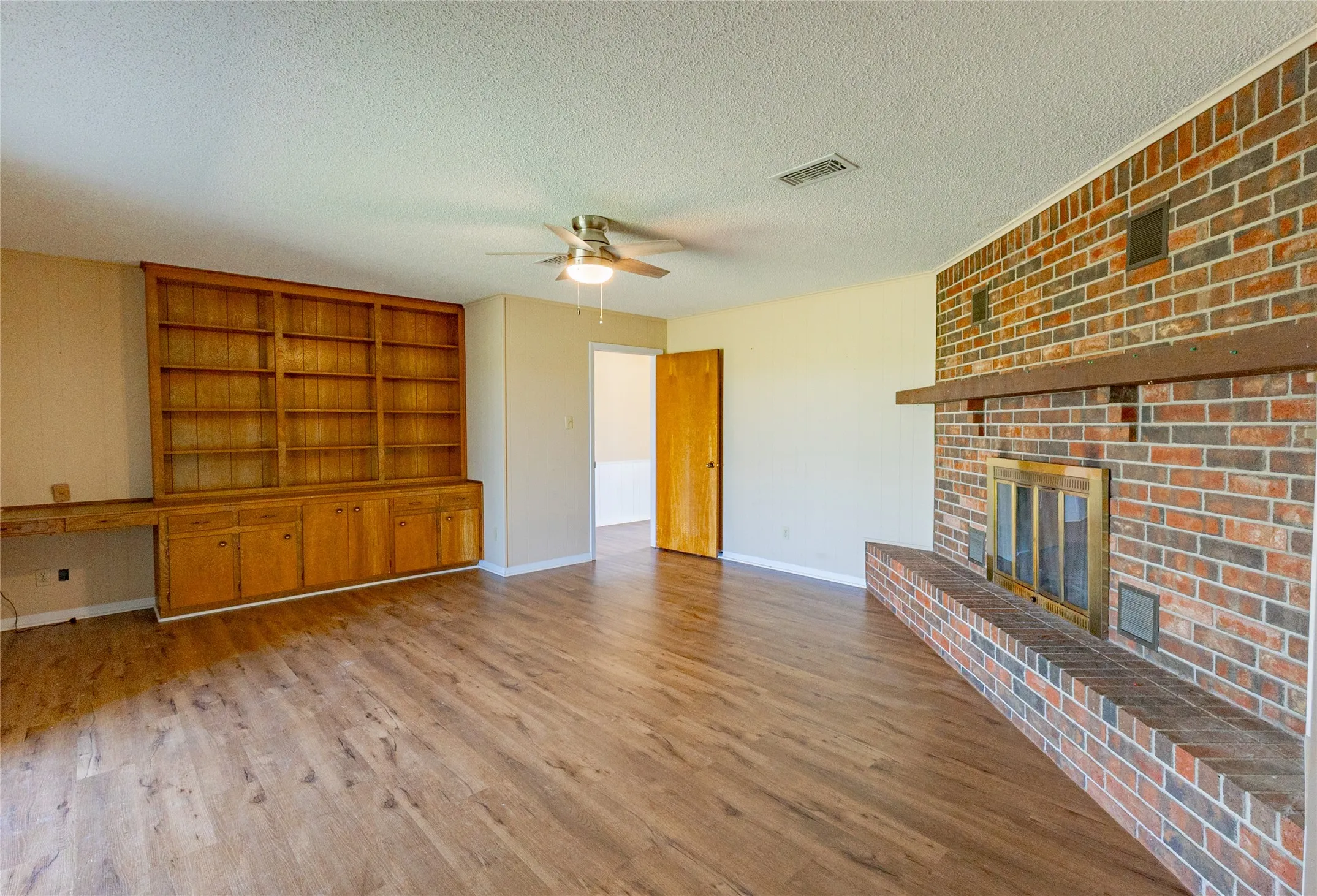 Unfurnished living room with a brick fireplace, light wood-style floors, a textured ceiling, a ceiling fan, and built in features