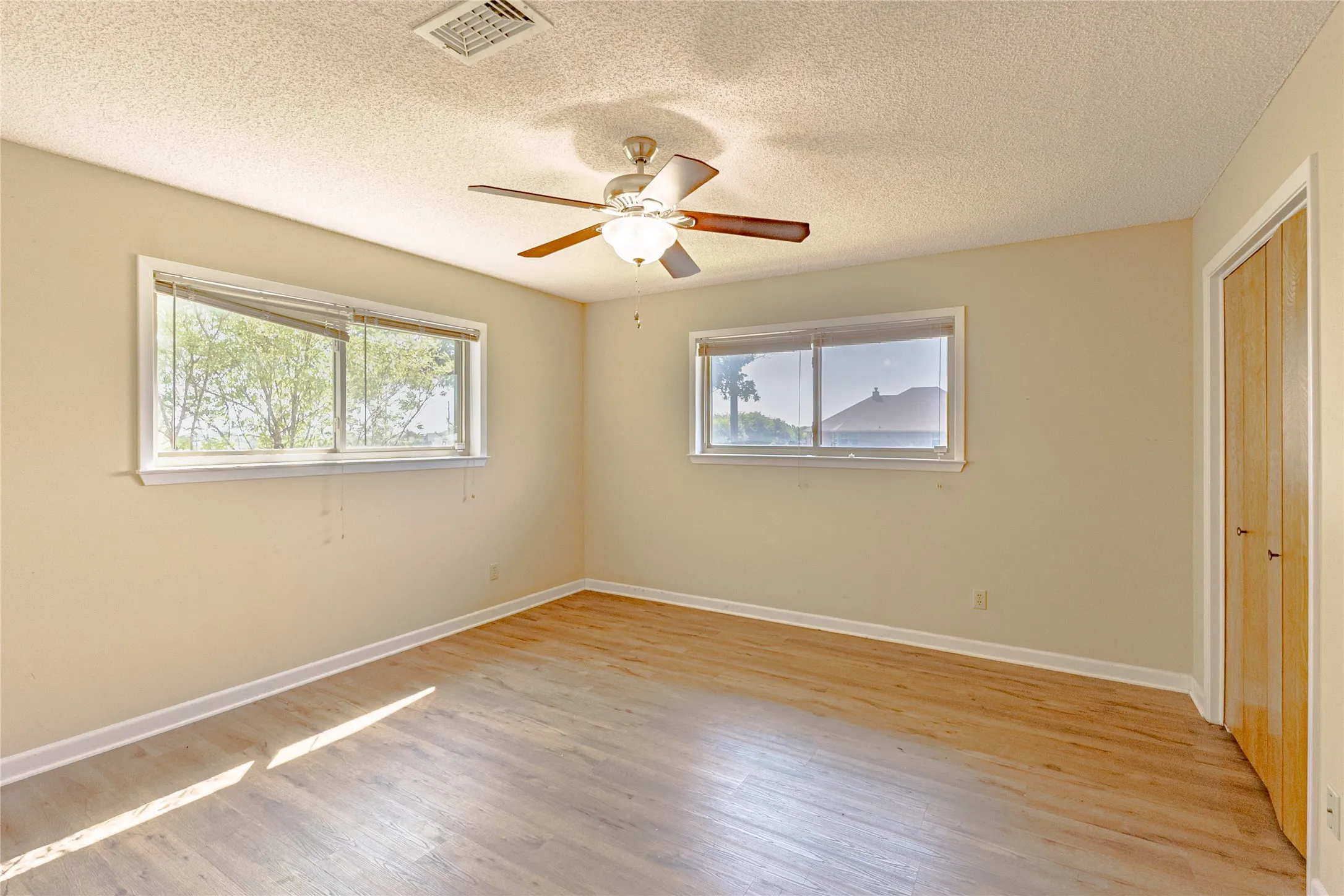 Unfurnished bedroom featuring a closet, light wood-style floors, a textured ceiling, and a ceiling fan