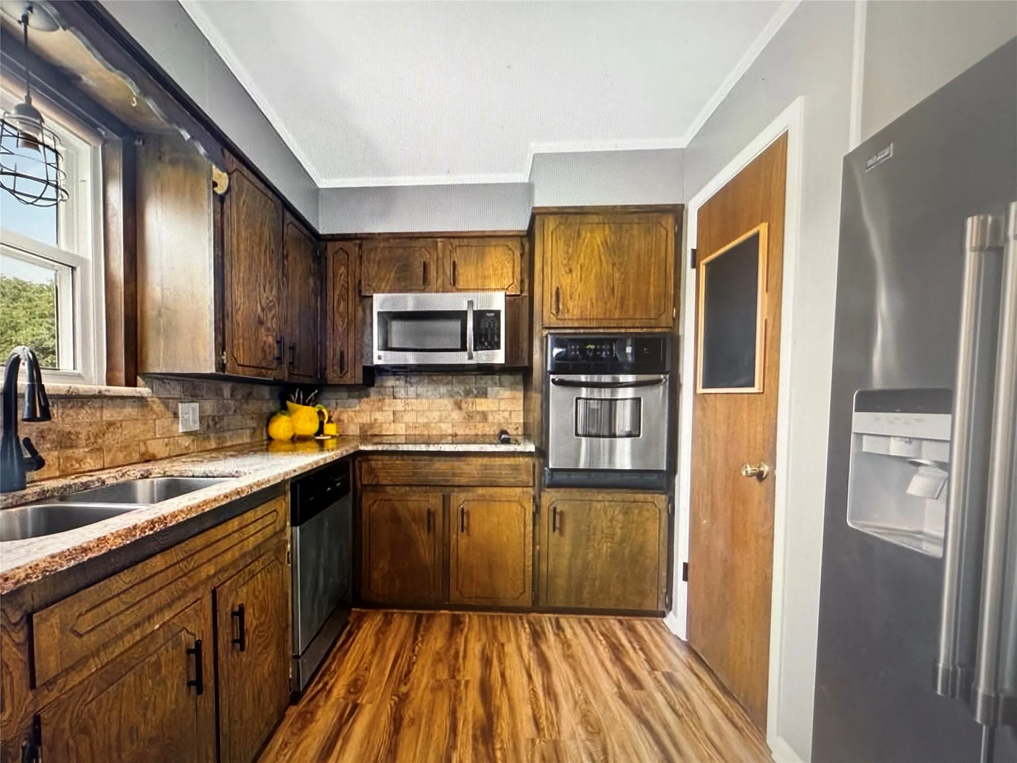 Kitchen featuring appliances with stainless steel finishes, decorative backsplash, dark wood-style floors, ornamental molding, and light stone counters