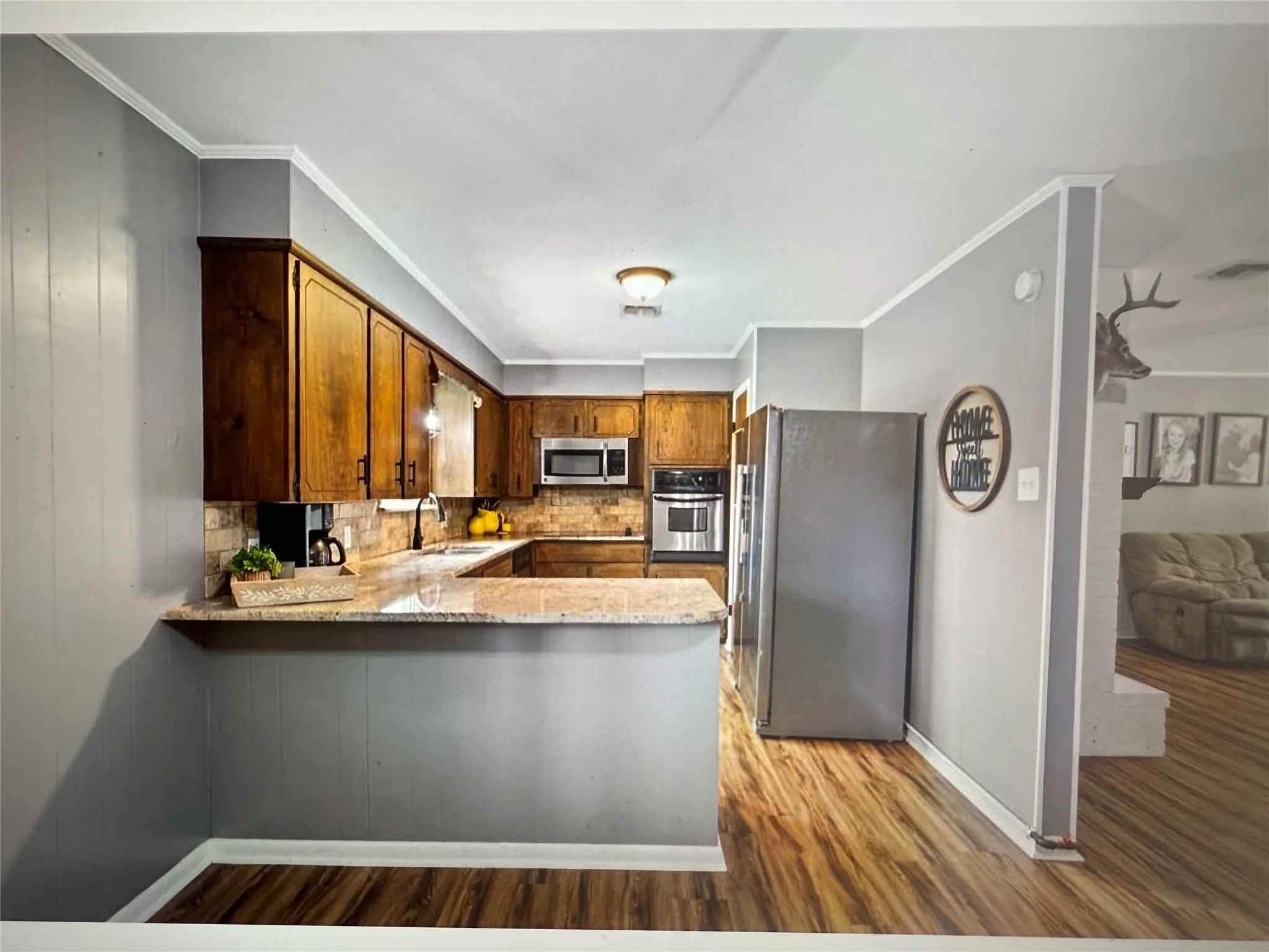 Kitchen with appliances with stainless steel finishes, decorative backsplash, light stone countertops, a peninsula, and light wood-type flooring
