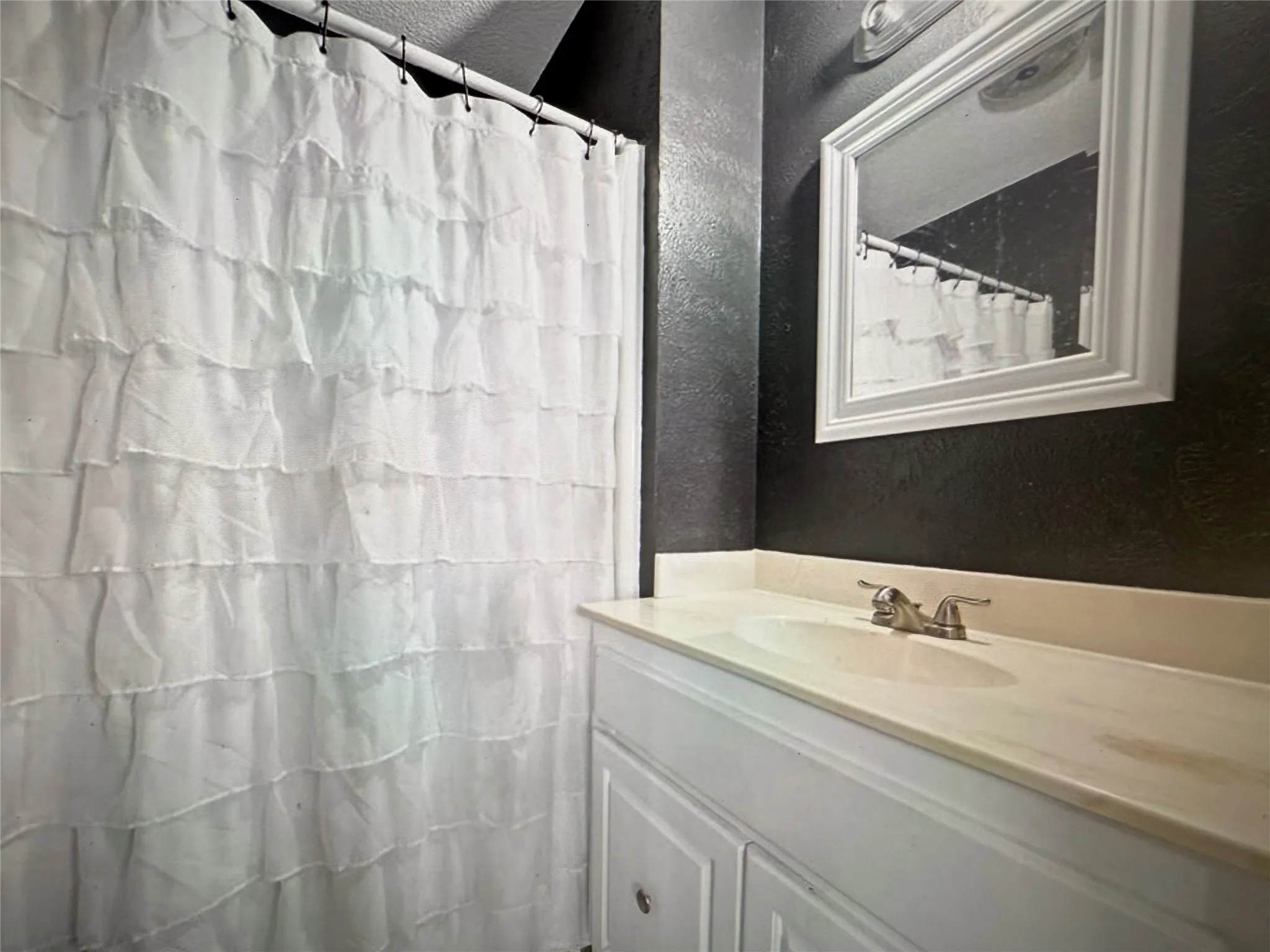 Full bathroom featuring a textured wall, vanity, and a shower with curtain