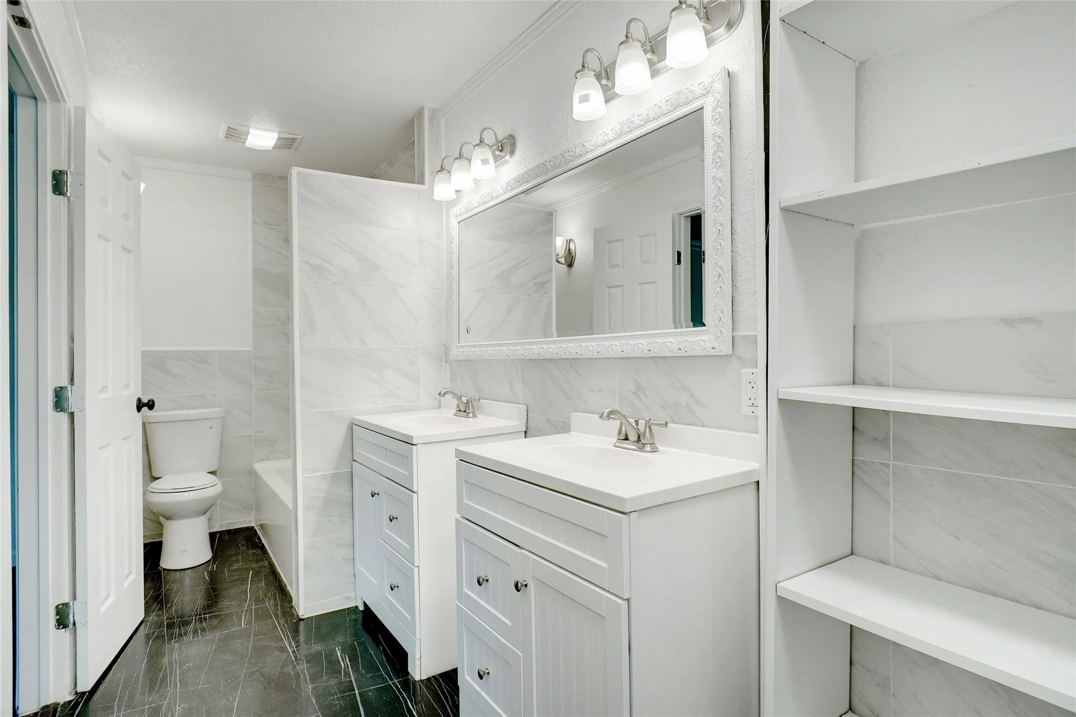 Full bath with tile walls, two vanities, and ornamental molding