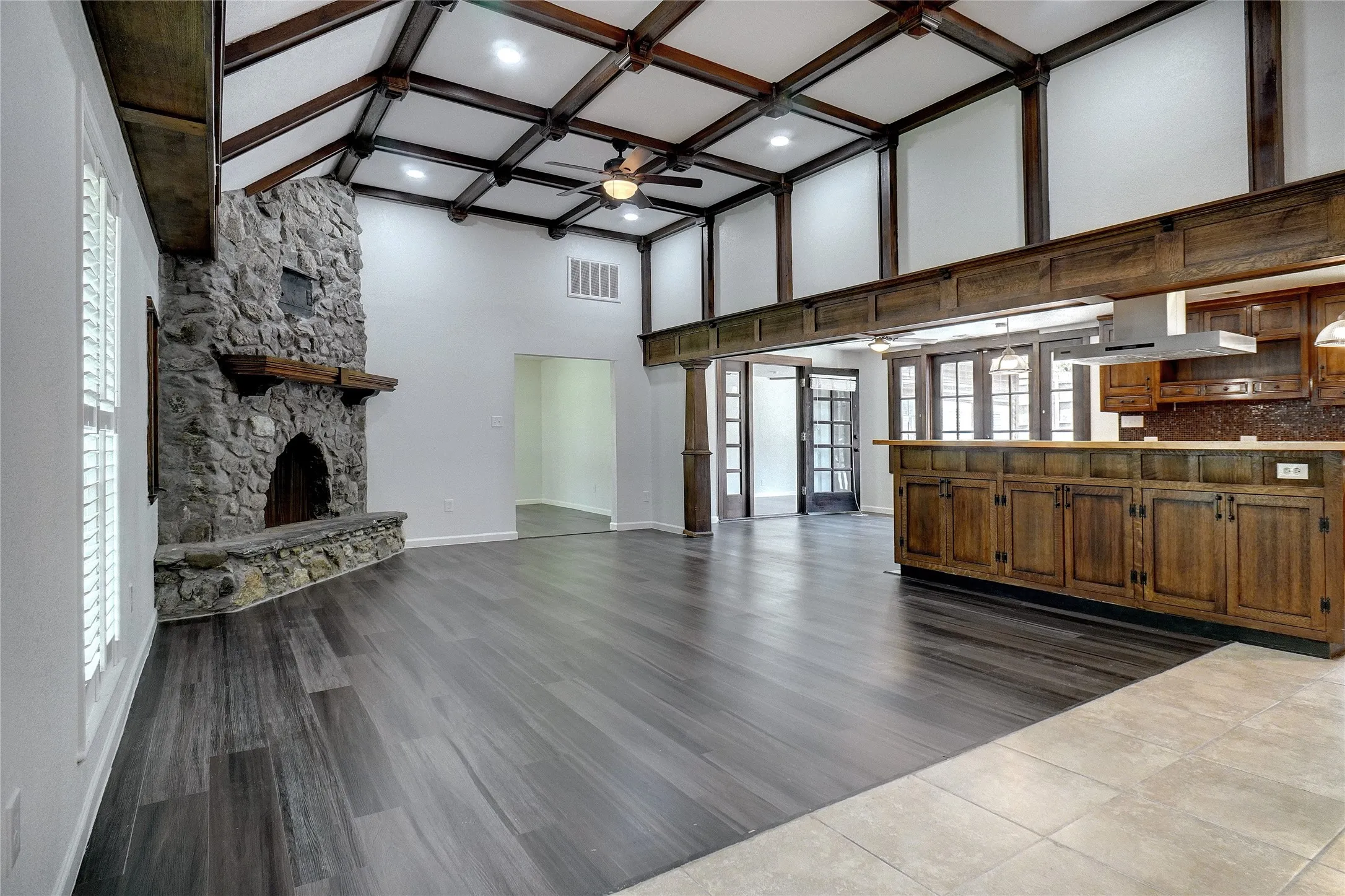 Unfurnished living room with a ceiling fan, beamed ceiling, dark wood-style flooring, a fireplace, and coffered ceiling
