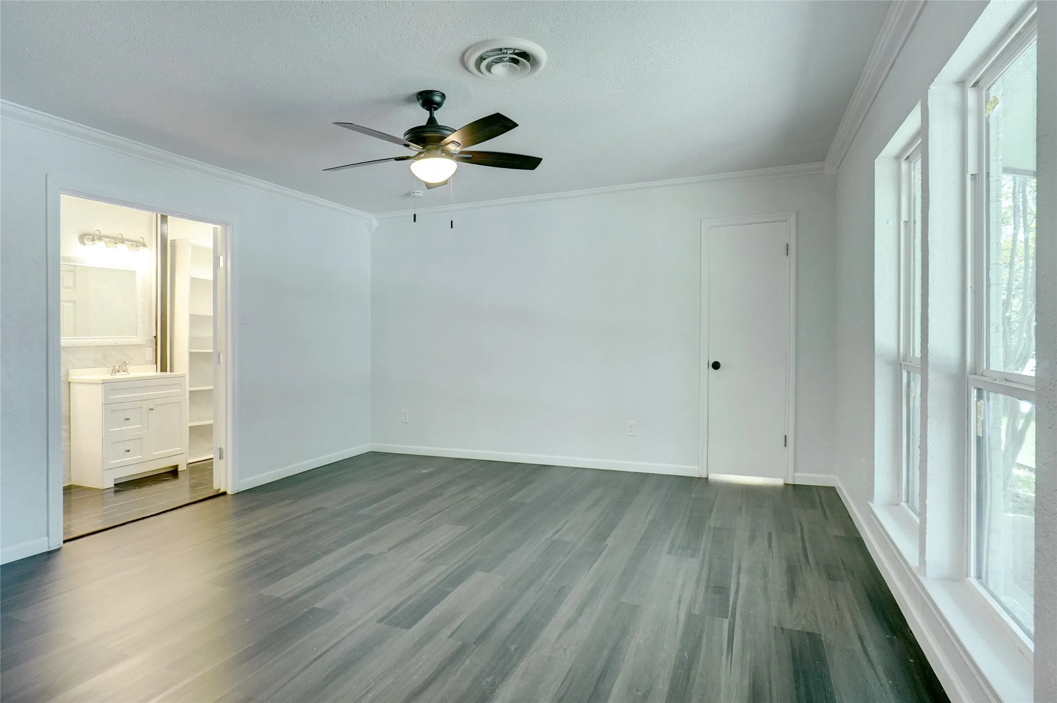 Unfurnished bedroom featuring ornamental molding, dark wood-type flooring, a ceiling fan, and connected bathroom