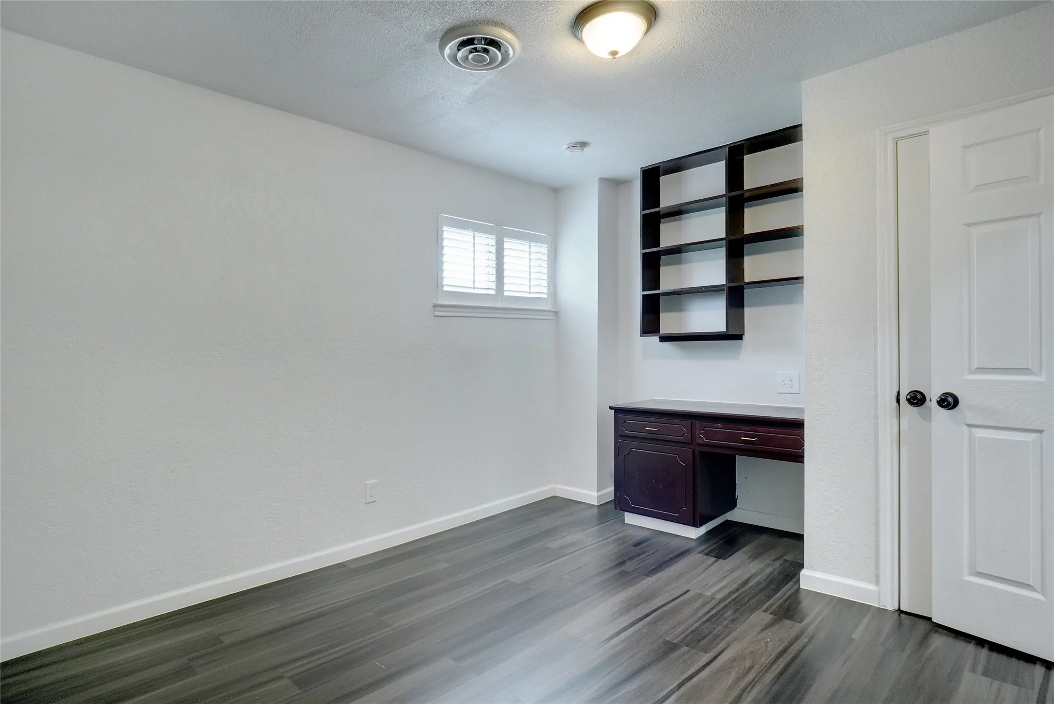 Unfurnished office featuring built in desk, dark wood finished floors, and a textured​​‌​​​​‌​​‌‌​‌‌​​​‌‌​‌​‌​‌​​​‌​​ ceiling