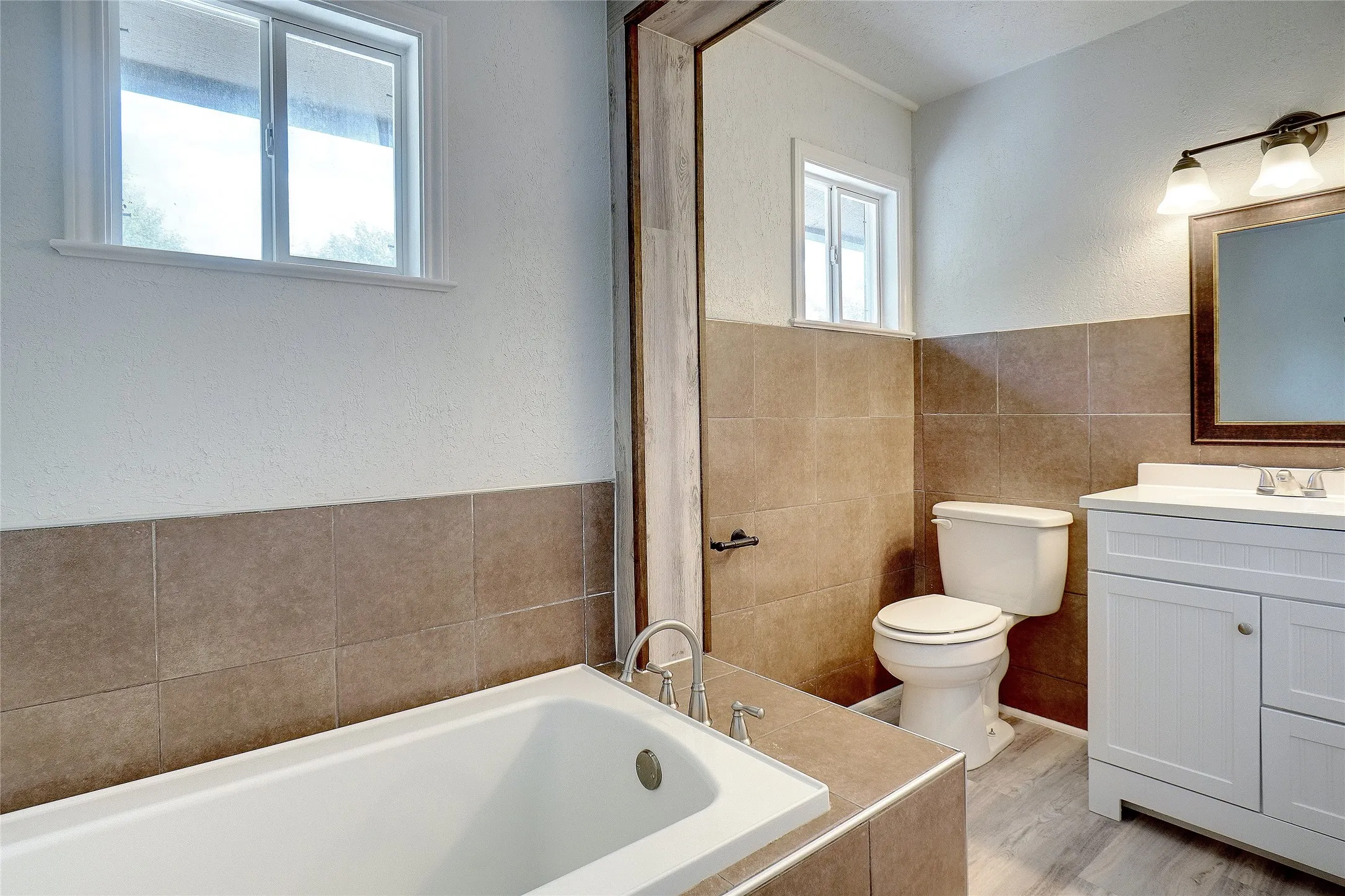 Bathroom featuring a textured wall, tiled tub, vanity, tile walls, and wood finished floors