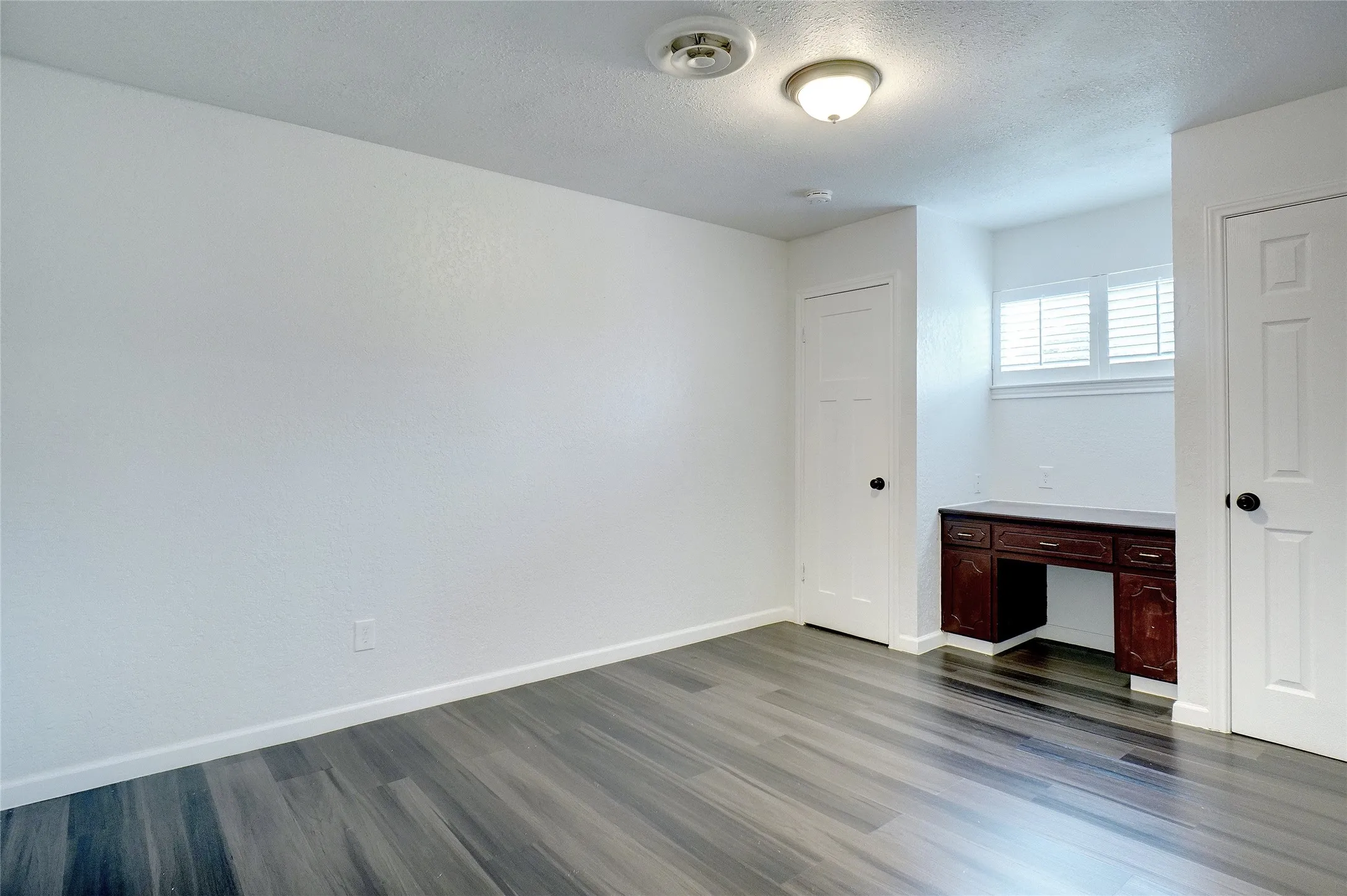 Unfurnished bedroom featuring built in study area, dark wood-style floors, and a textured ceiling