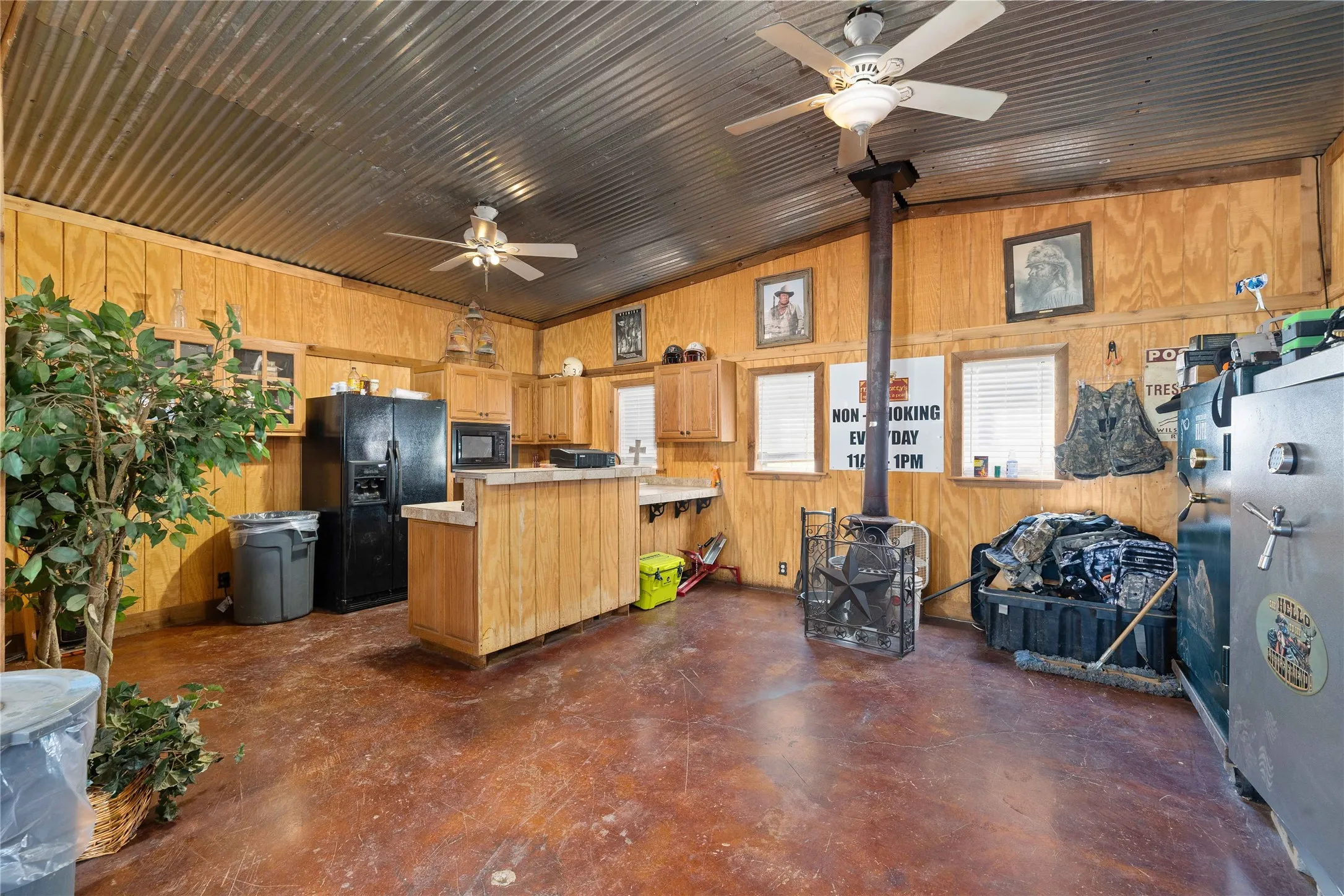 Kitchen with light countertops, black appliances, finished concrete flooring, wooden walls, and a peninsula