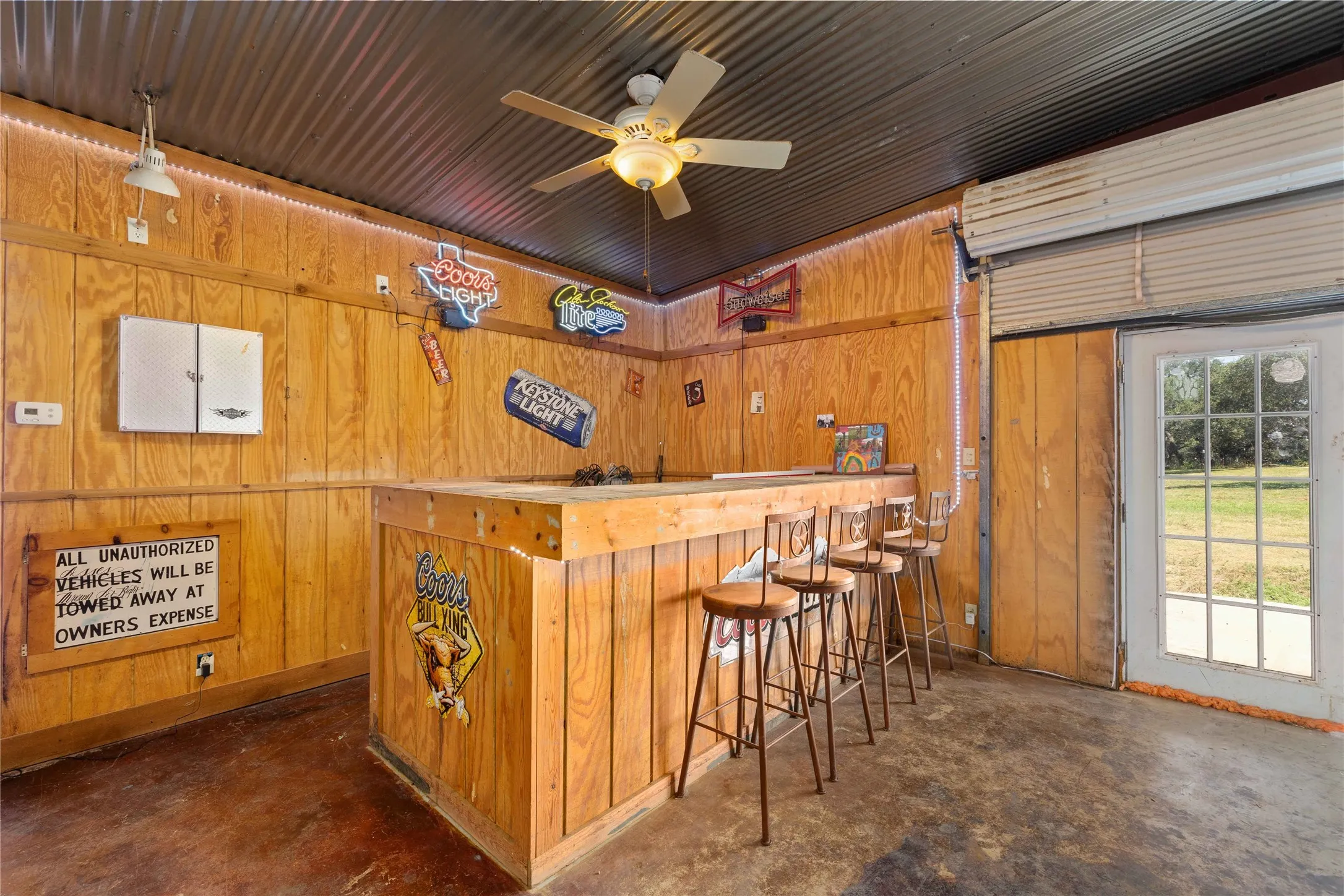 Indoor dry bar with wood walls, concrete floors, hanging light fixtures, and a ceiling fan