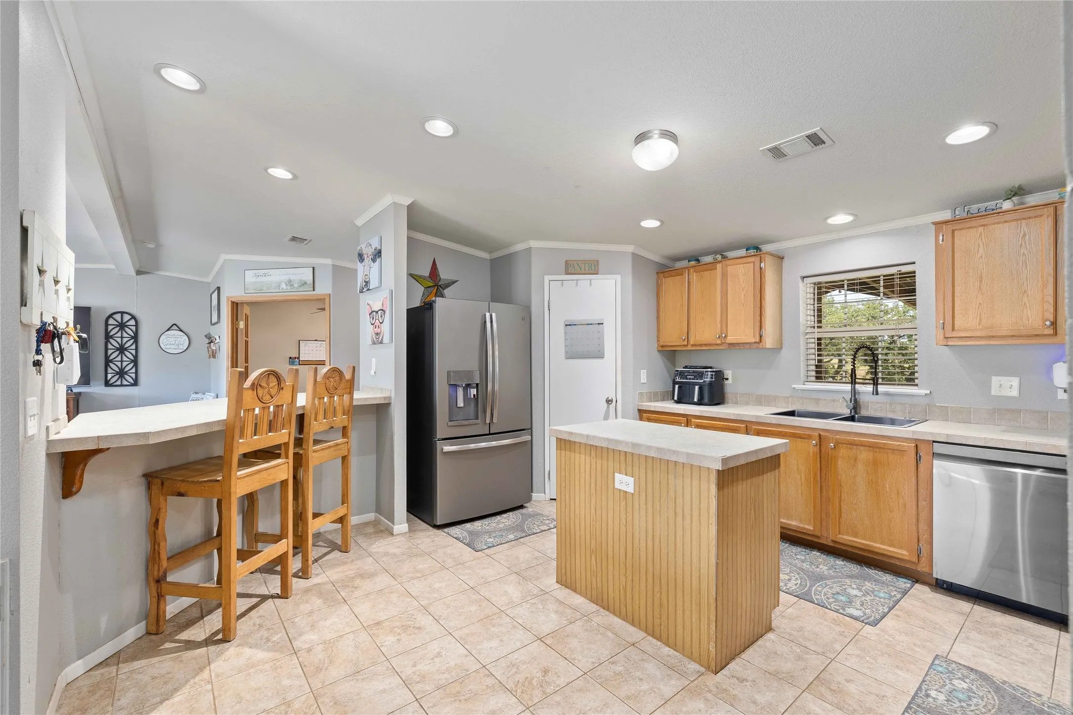 Kitchen with light countertops, appliances with stainless steel finishes, a kitchen island, ornamental molding, and recessed lighting