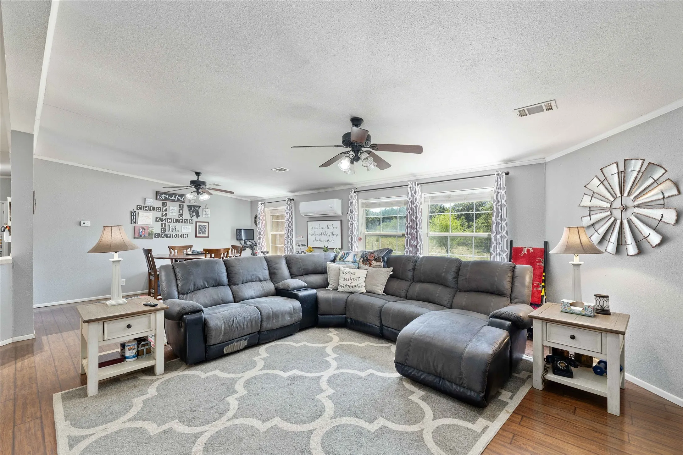 Living room featuring hardwood / wood-style flooring, ornamental molding, ceiling fan, a wall unit AC, and a textured ceiling
