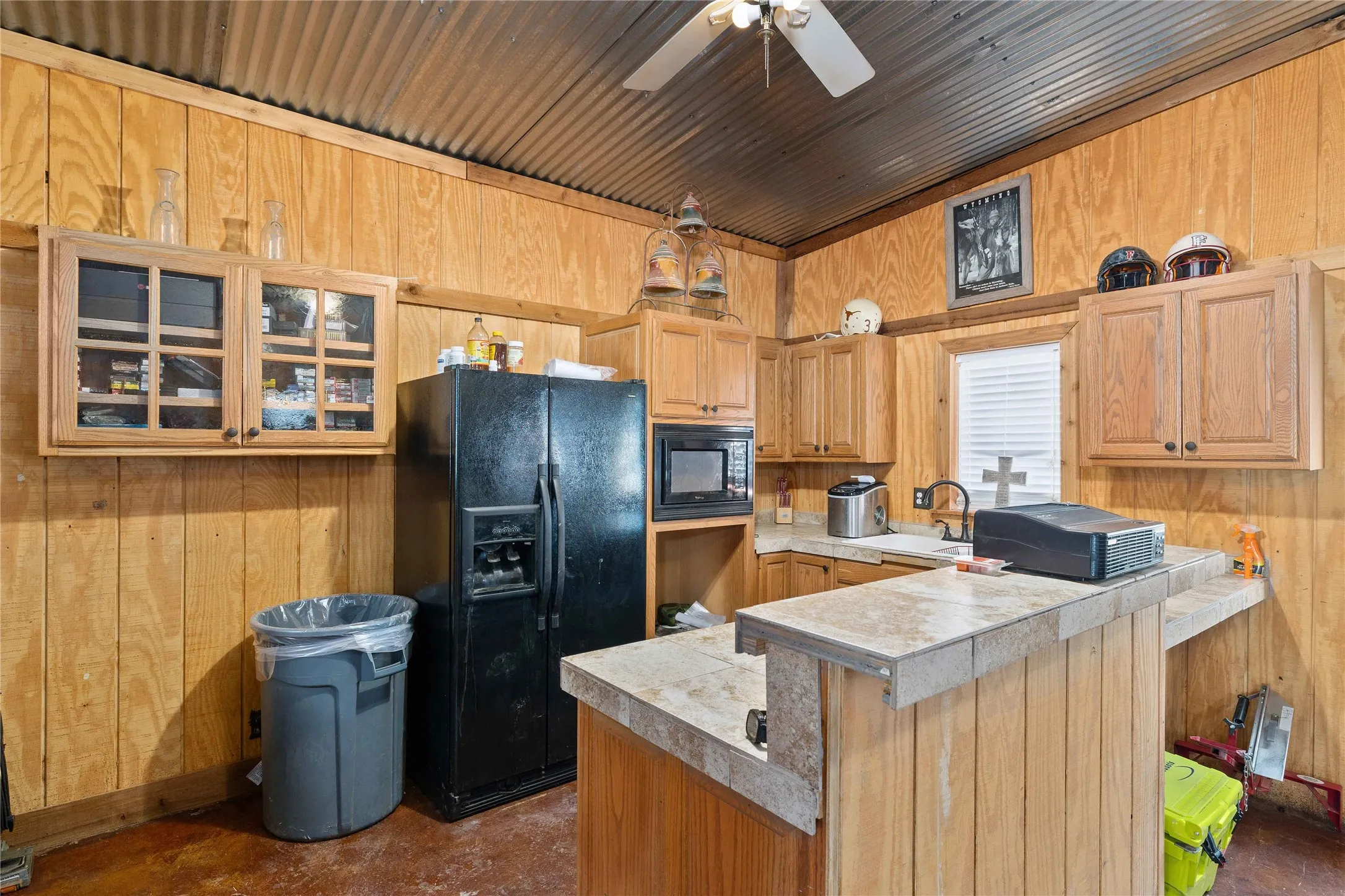 Kitchen featuring wooden walls, black appliances, concrete floors, glass insert cabinets, and a breakfast bar