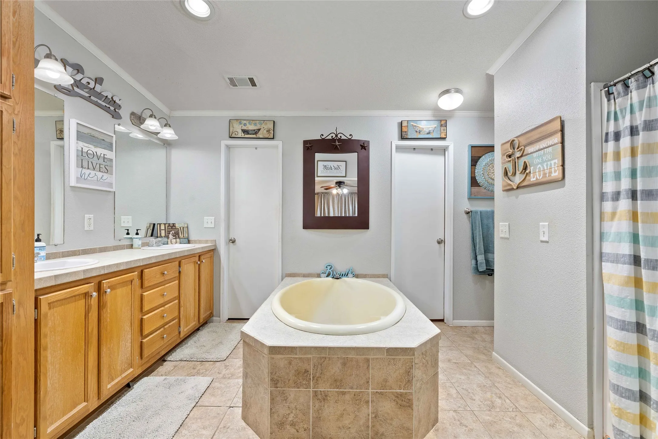 Bathroom featuring ornamental molding, a bath, double vanity, light tile patterned flooring, and curtained shower