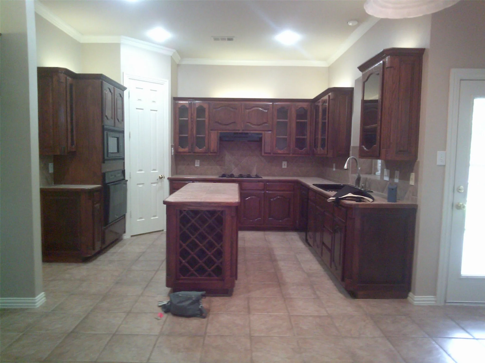 Kitchen featuring decorative backsplash, glass insert cabinets, a kitchen island, black appliances, and light countertops