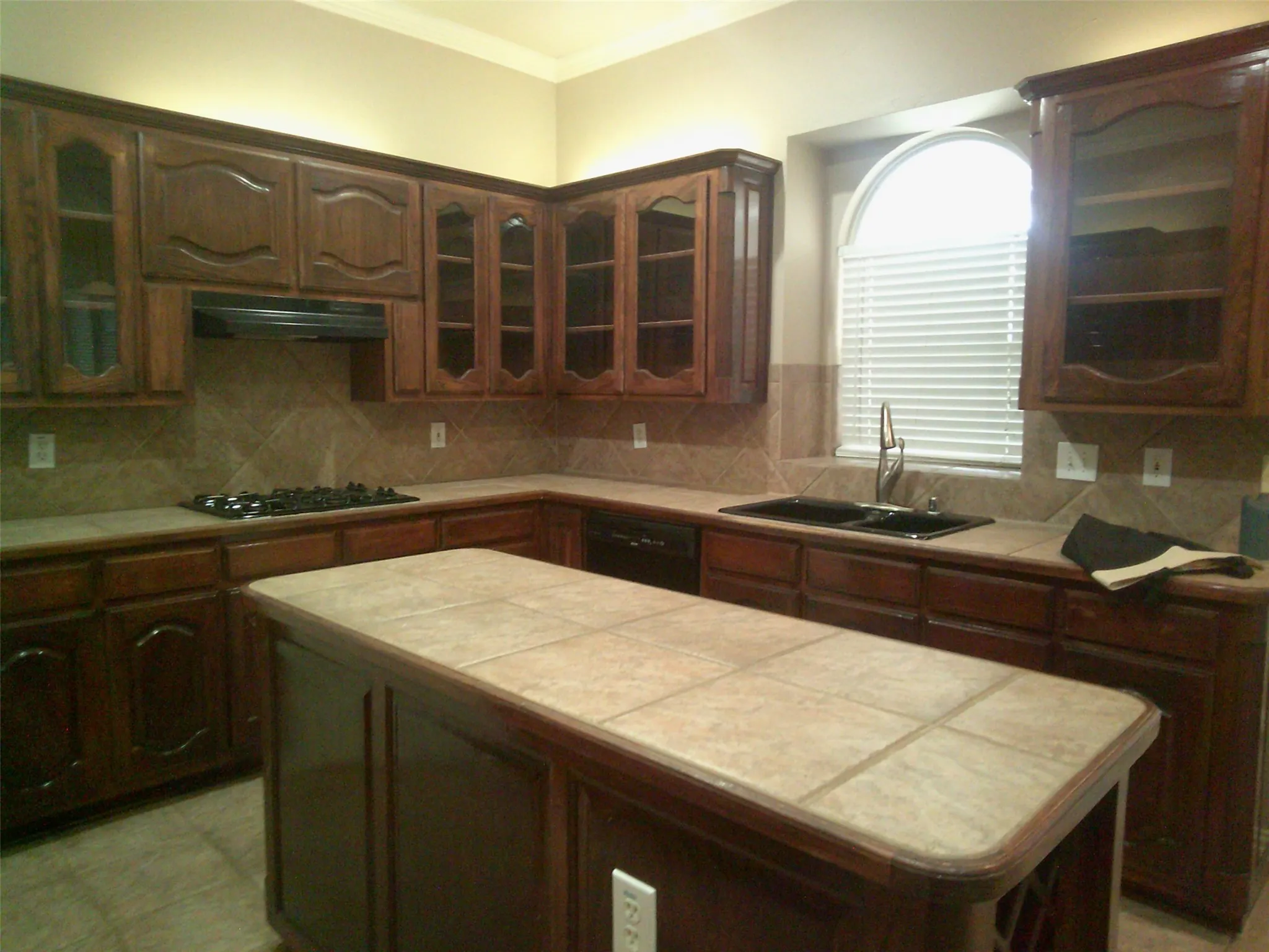 Kitchen featuring glass insert cabinets, tasteful backsplash, light countertops, crown molding, and exhaust hood