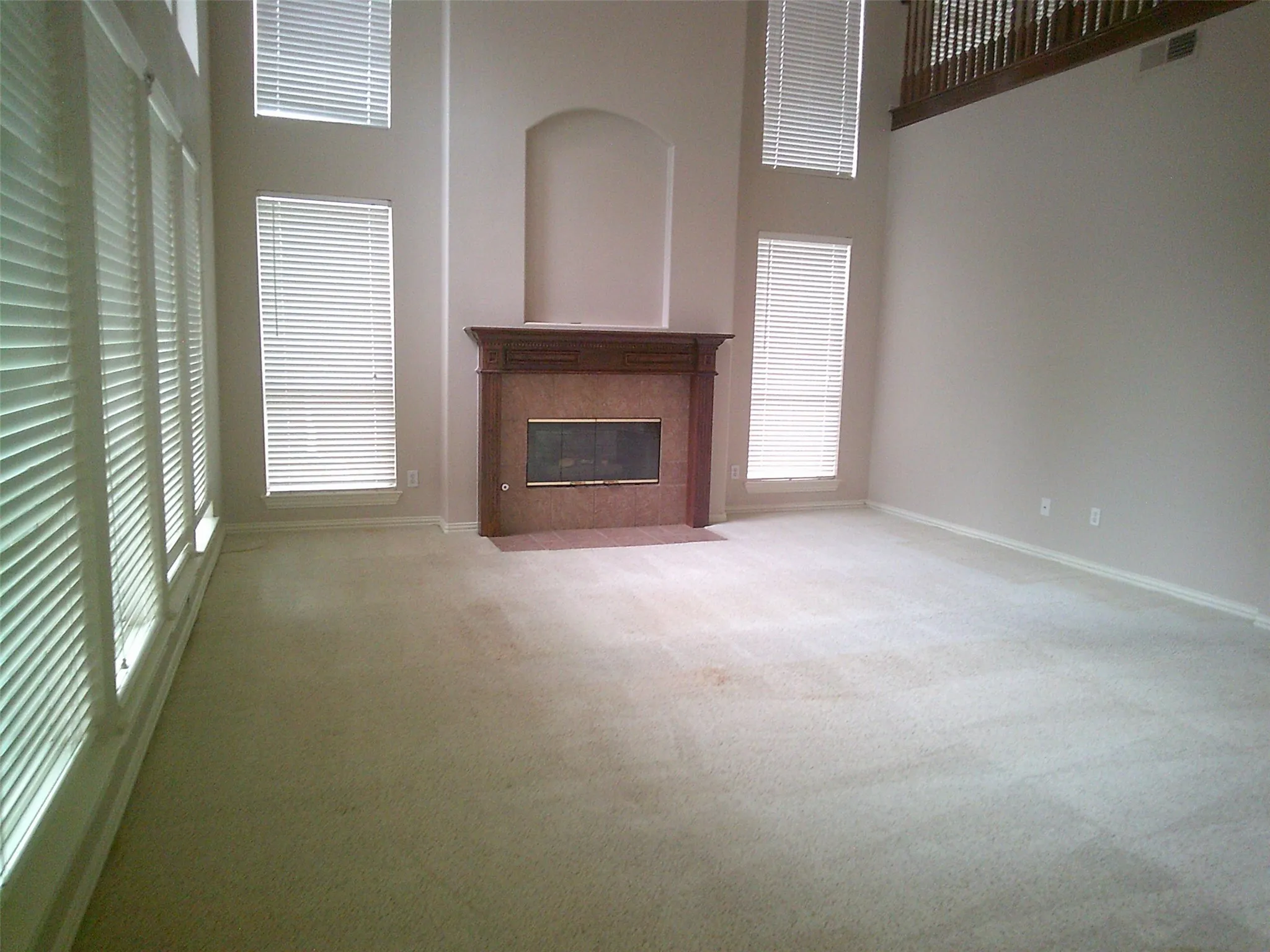Unfurnished living room featuring a high ceiling, light colored carpet, and a tiled fireplace