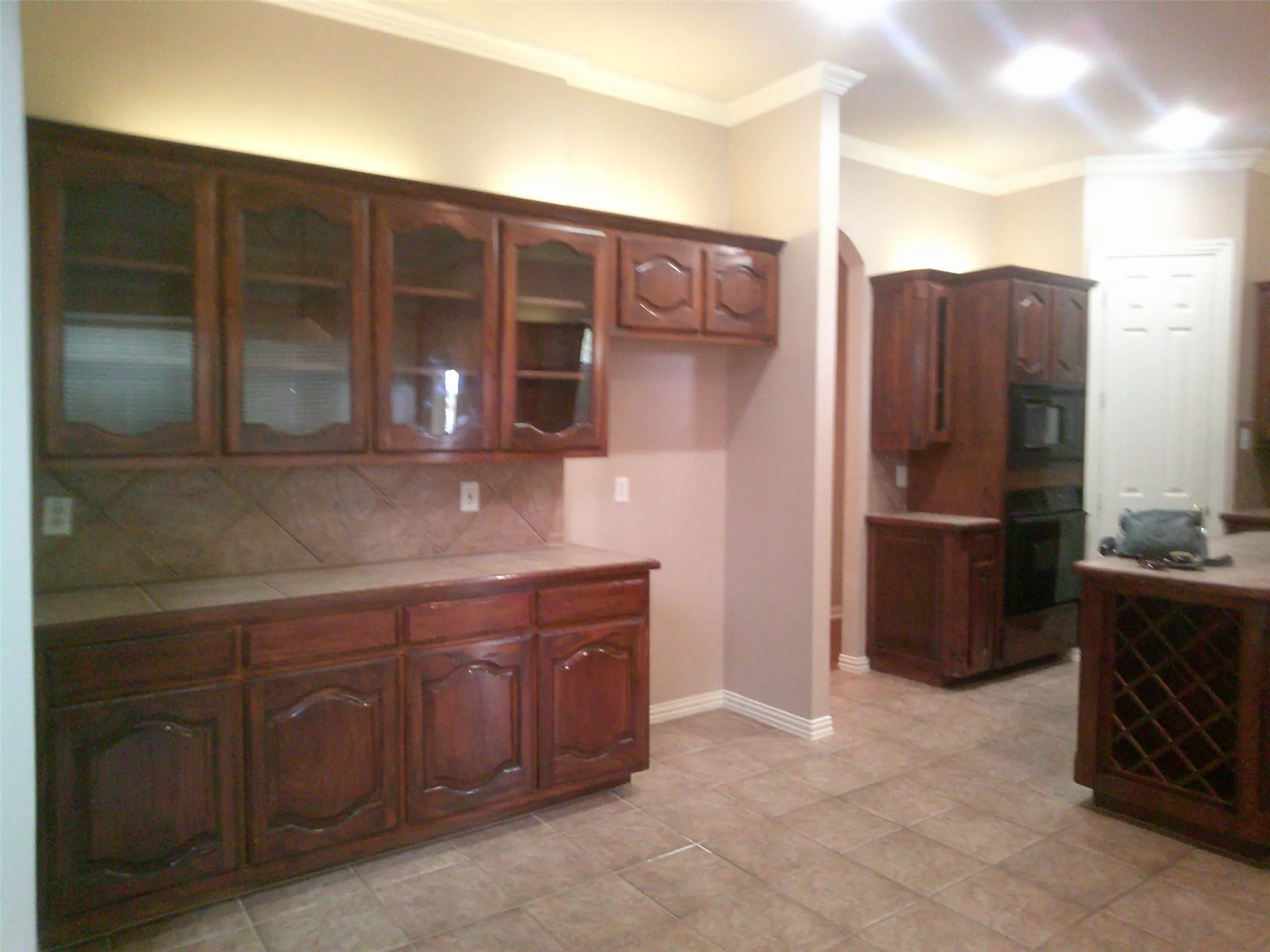 Kitchen featuring crown molding, glass insert cabinets, tasteful backsplash, black appliances, and tile counters