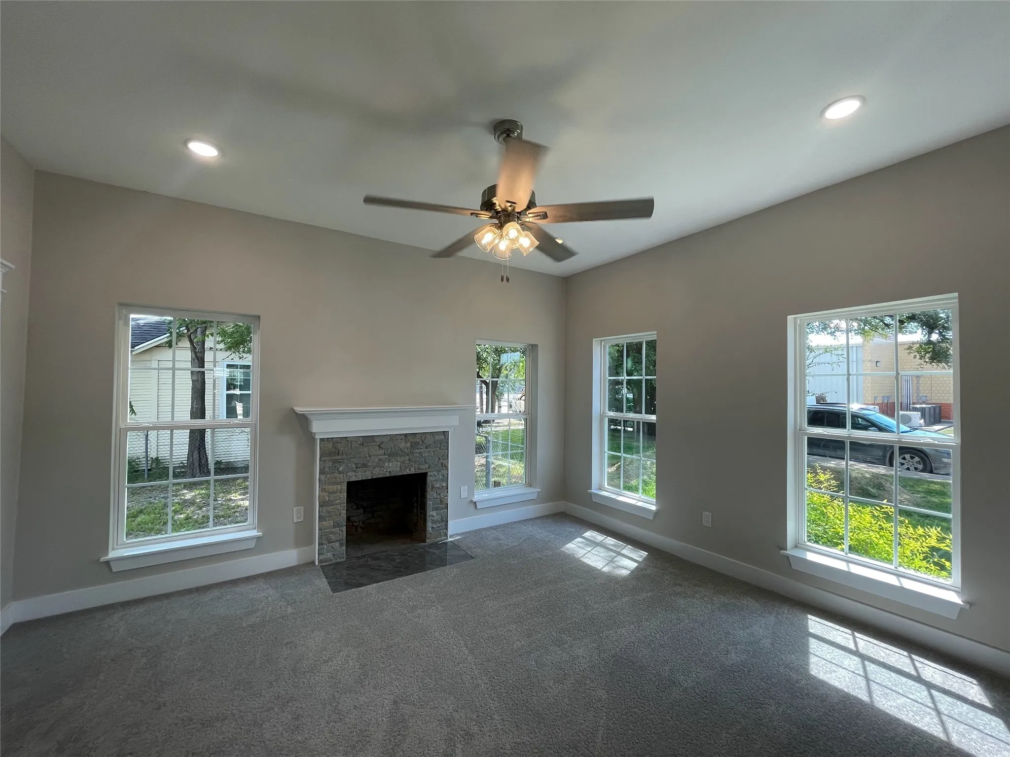 Unfurnished living room with healthy amount of natural light, recessed lighting, a stone fireplace, carpet, and ceiling fan