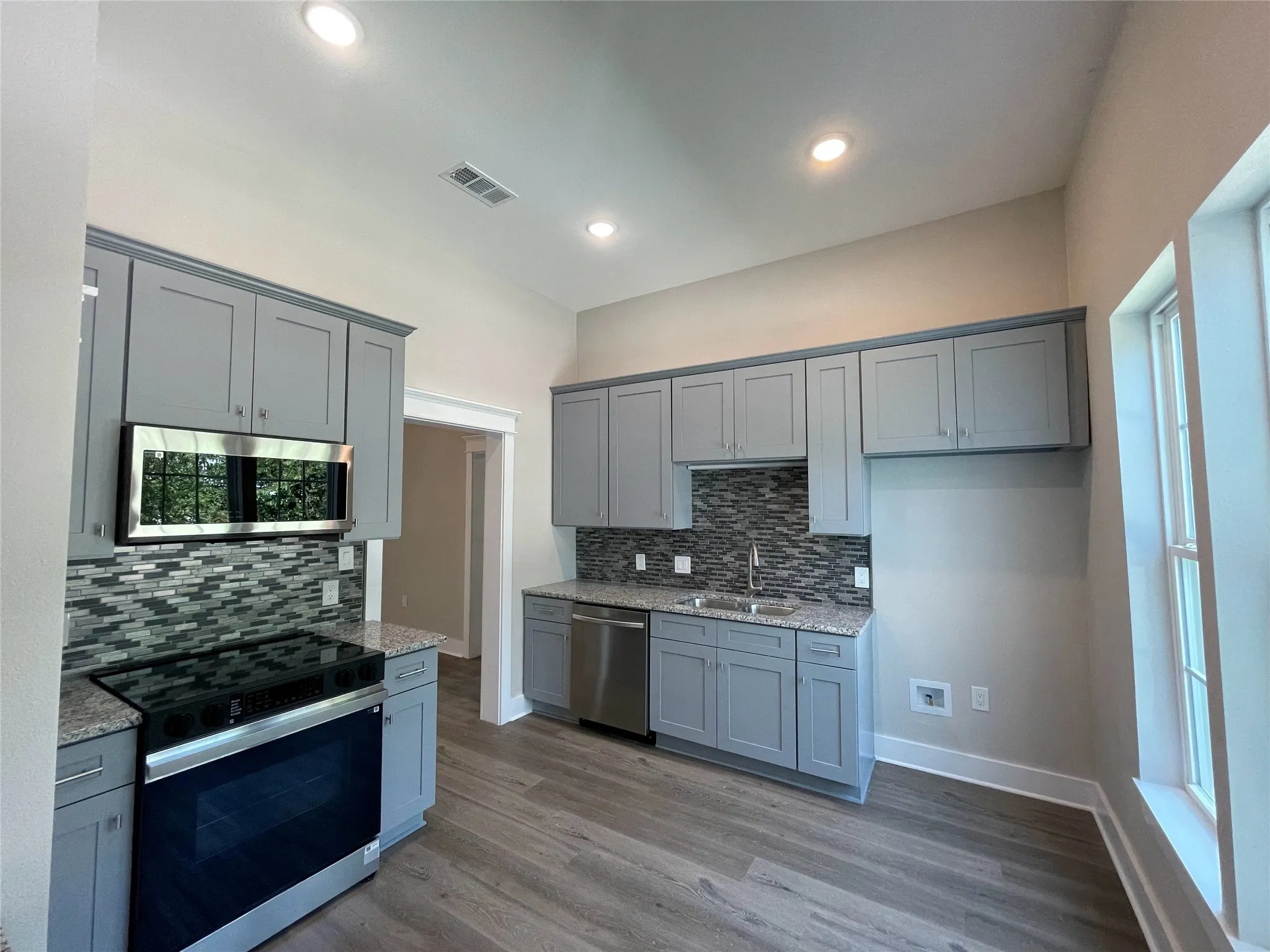 Kitchen with appliances with stainless steel finishes, gray cabinets, light stone countertops, dark wood-style floors, and recessed lighting