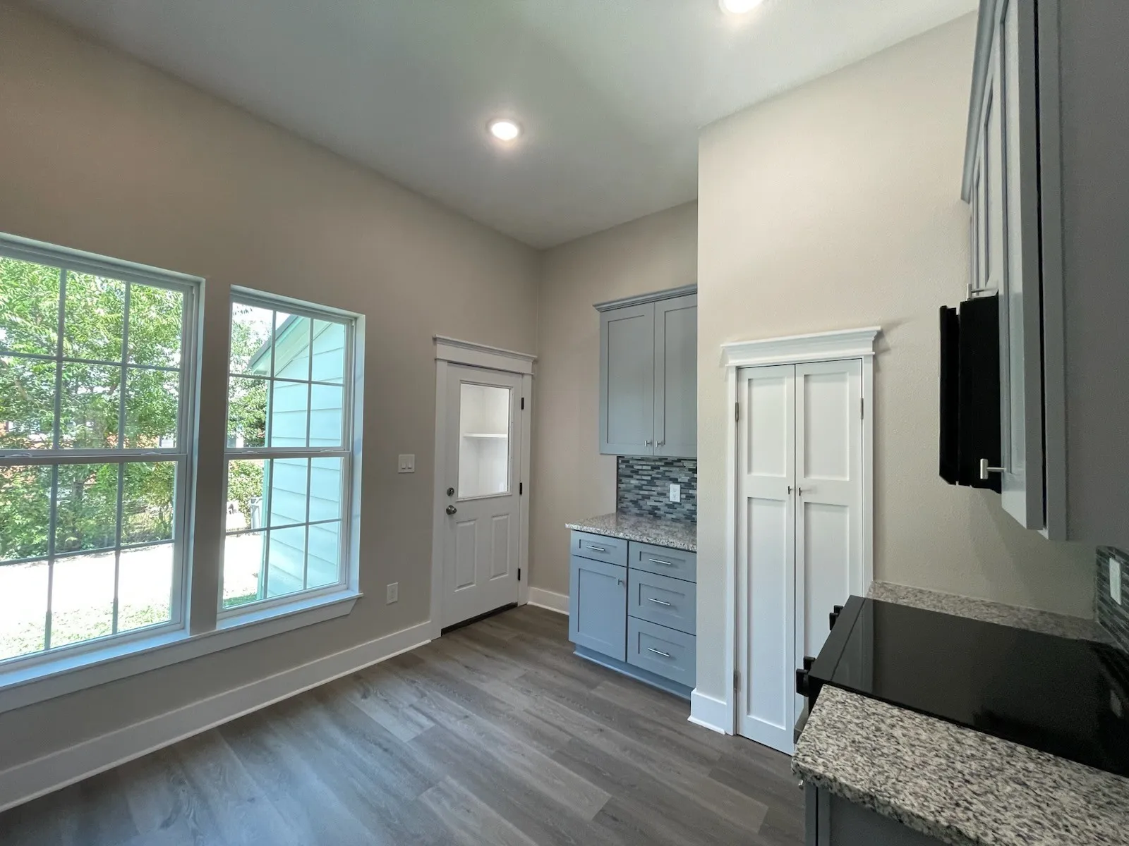 Kitchen with gray cabinets, dark wood-type flooring, light stone counters, black / electric stove, and backsplash