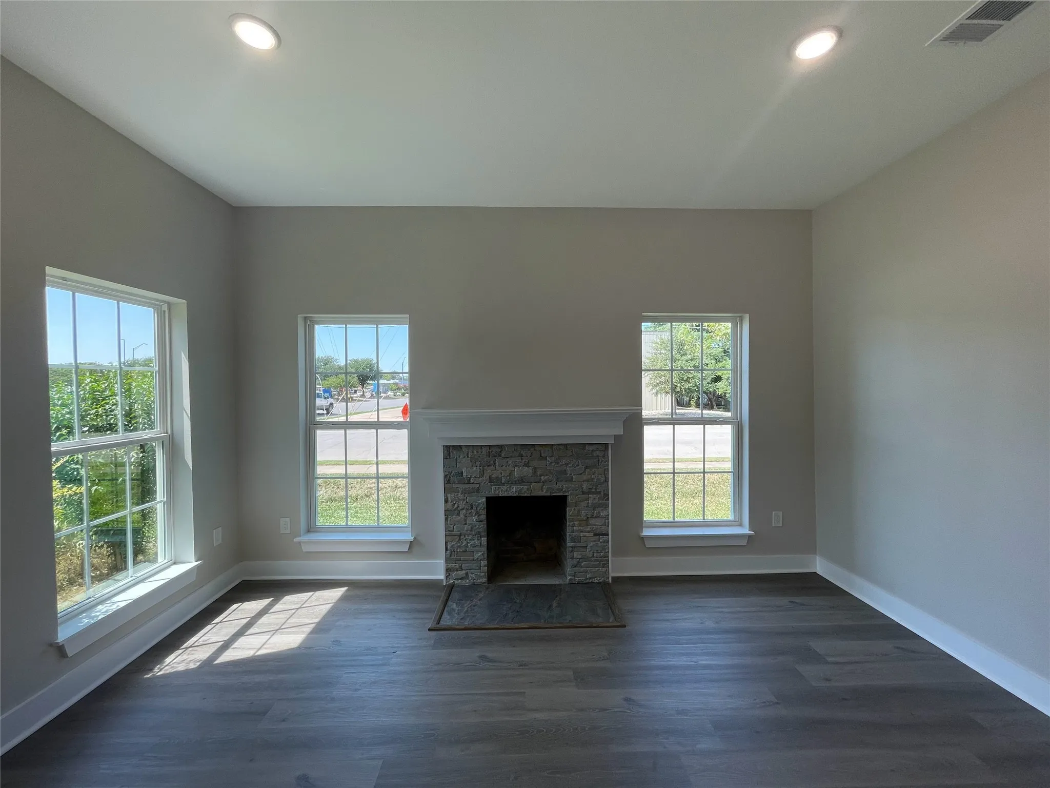Unfurnished living room with recessed lighting, dark wood-style flooring, and a stone fireplace