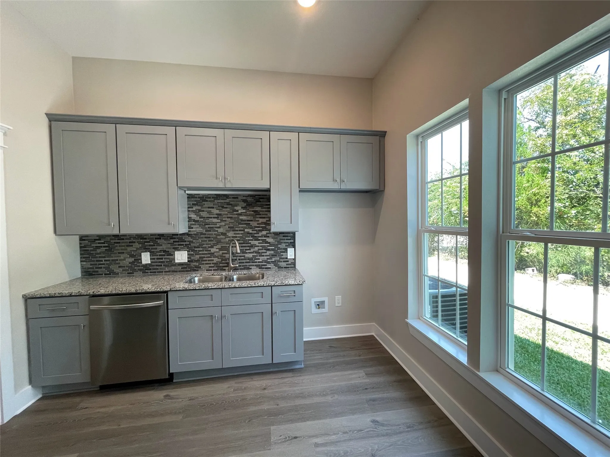 Kitchen with gray cabinets, stainless steel dishwasher, light stone counters, backsplash, and recessed lighting