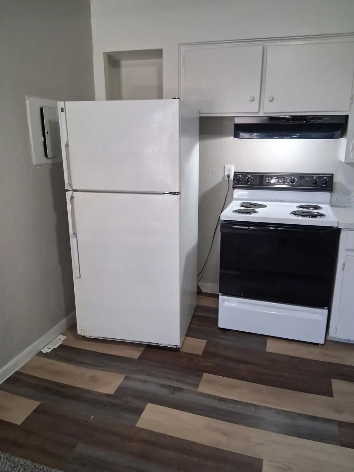 Kitchen featuring electric stove, freestanding refrigerator, white cabinetry, range hood, and light countertops