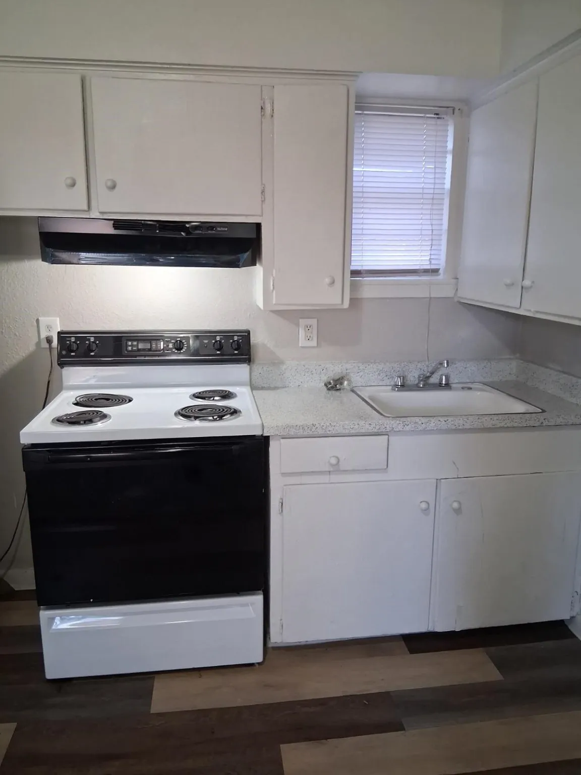 Kitchen with electric stove, light countertops, white cabinets, under cabinet range hood, and dark wood-style flooring