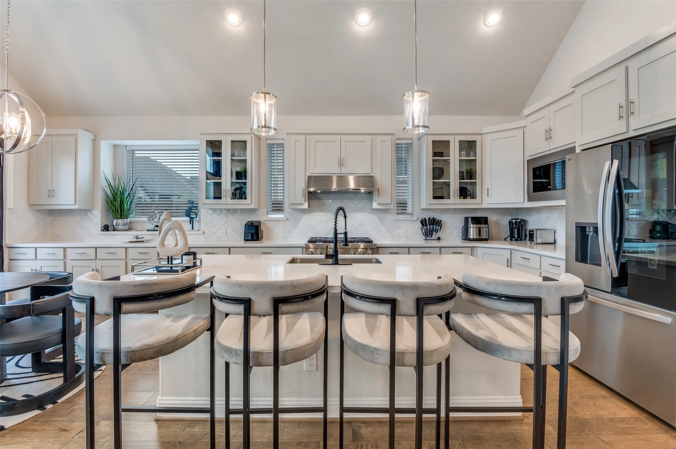 Kitchen with glass insert cabinets, lofted ceiling, hanging light fixtures, appliances with stainless steel finishes, and tasteful backsplash
