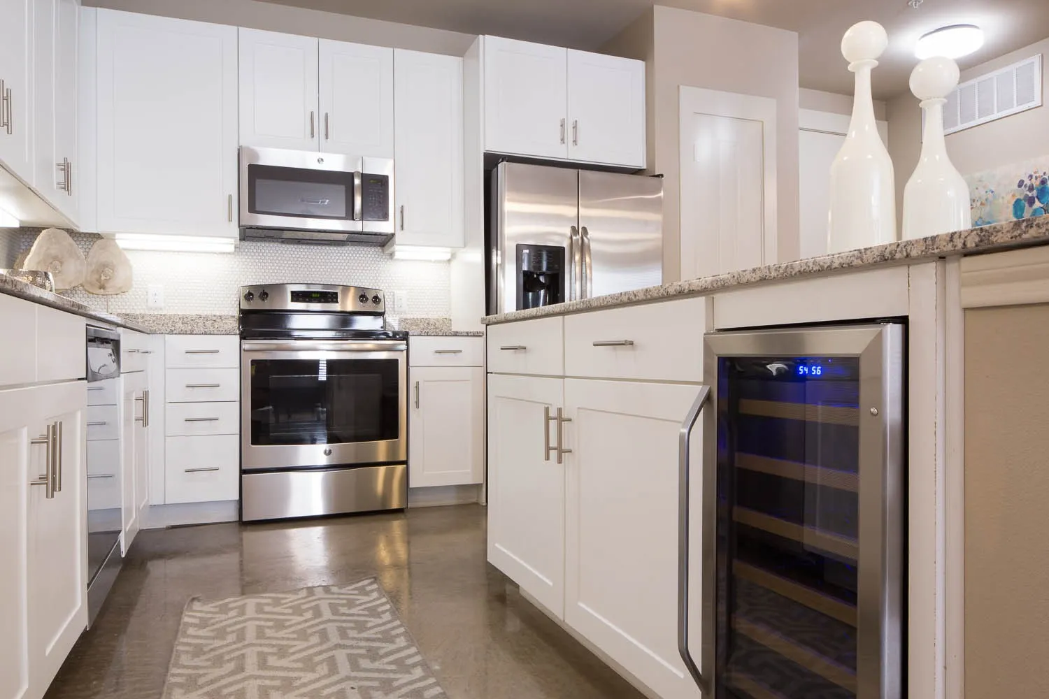 Kitchen featuring stainless steel appliances, white cabinets, wine cooler, backsplash, and light stone counters