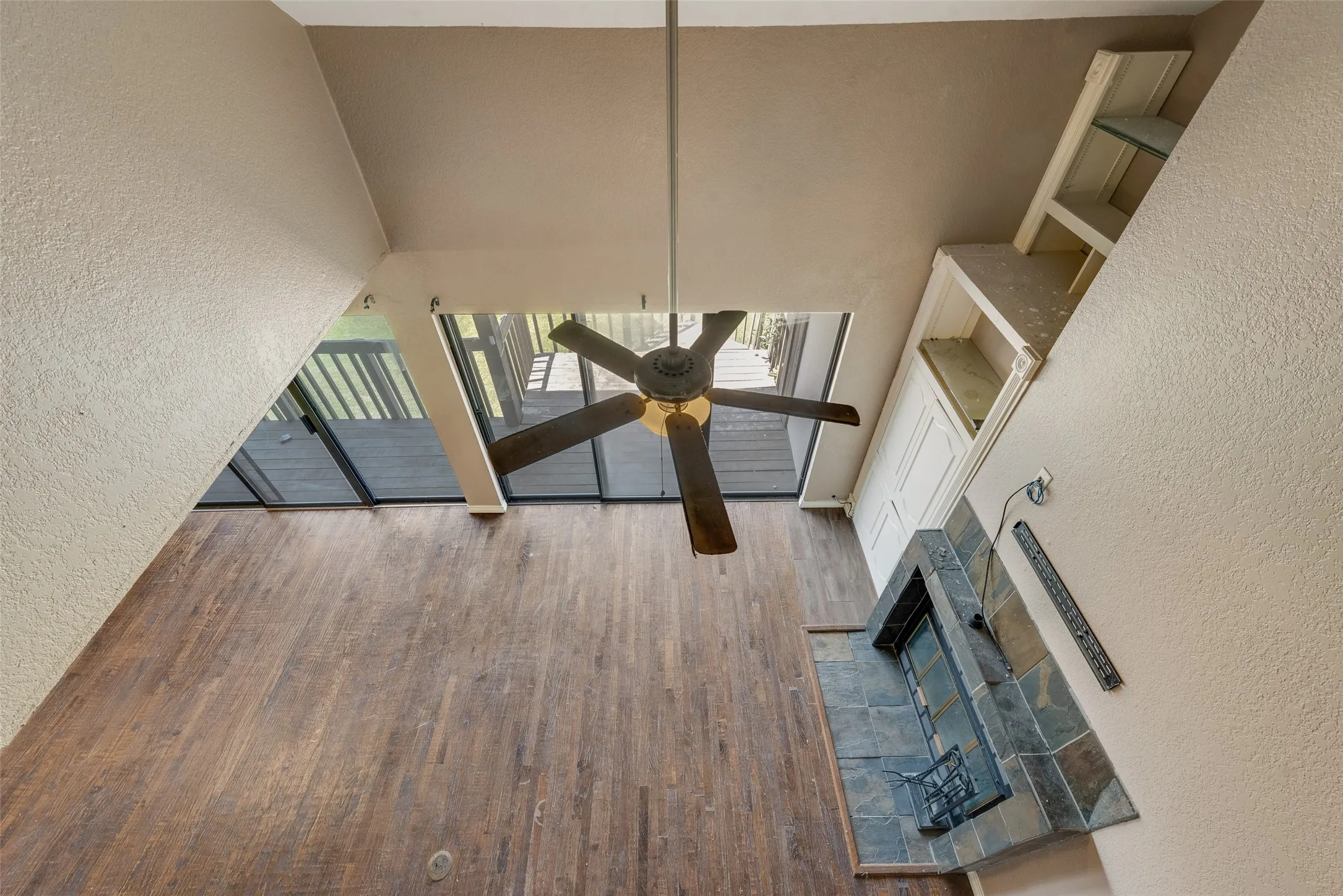 Unfurnished living room featuring a textured wall, wood finished floors, a high ceiling, a fireplace, and a ceiling fan