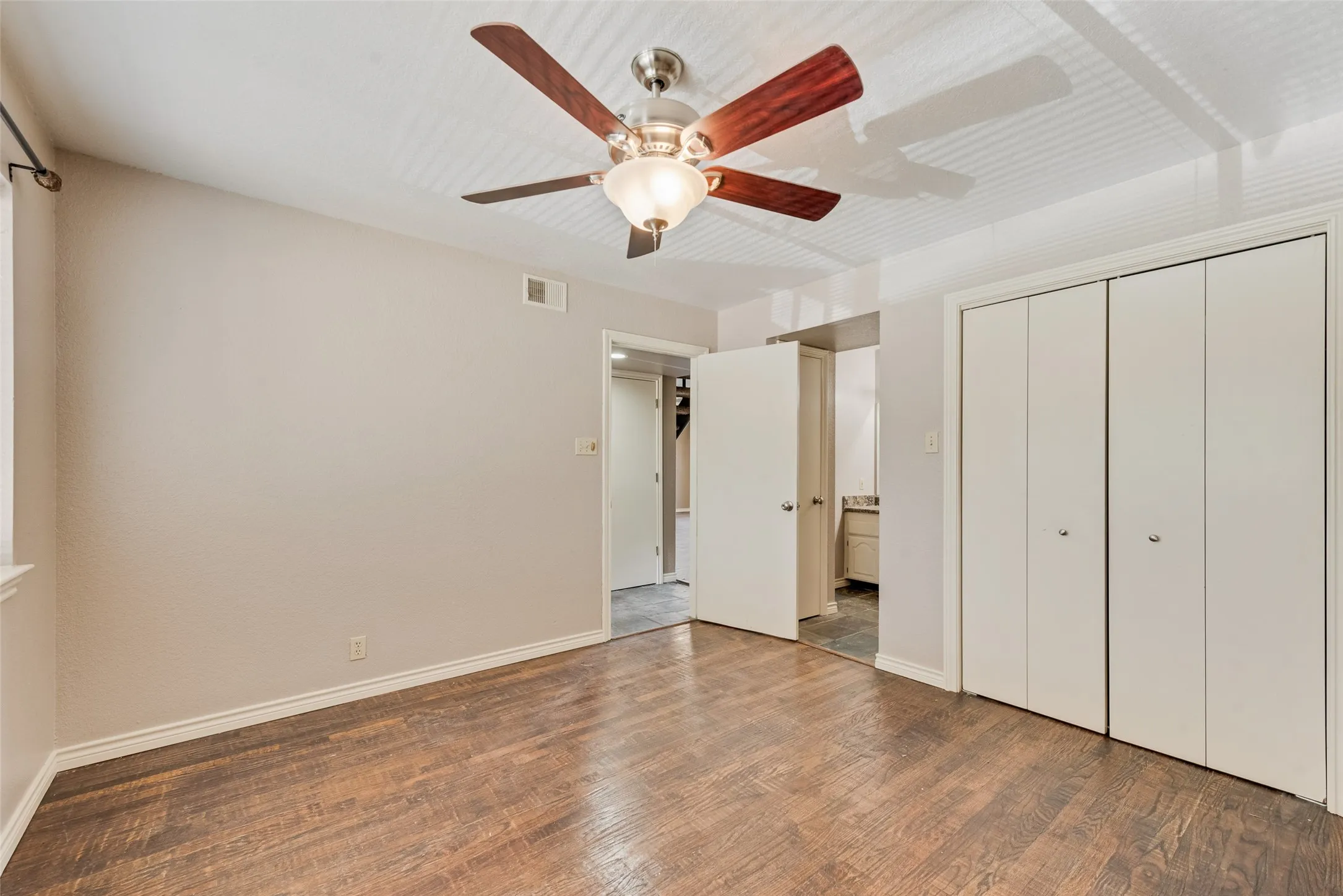 Unfurnished bedroom featuring wood finished floors, a ceiling fan, a closet, and ensuite bathroom