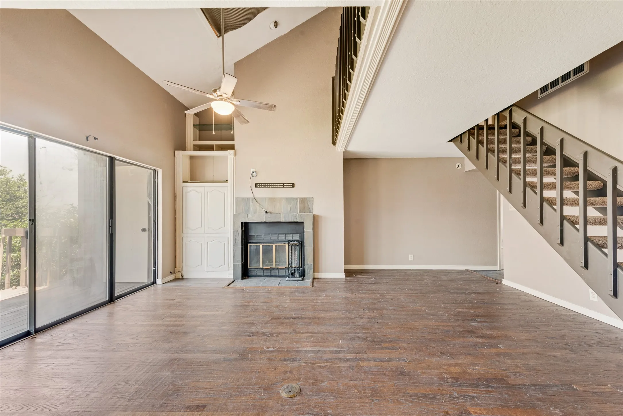 Unfurnished living room with high vaulted ceiling, a fireplace, wood finished floors, stairway, and a ceiling fan